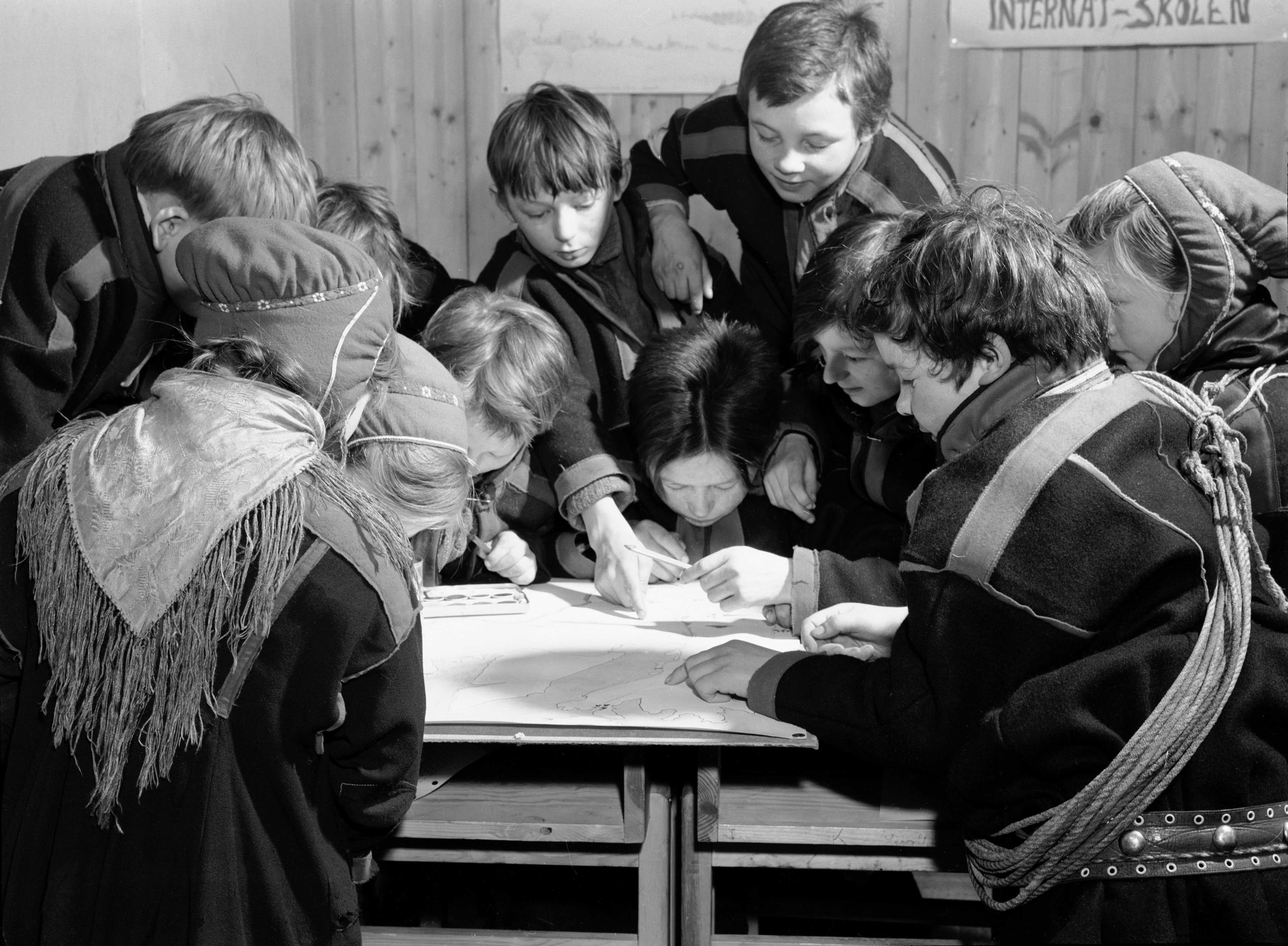 Karasjok, Finnmark, januar 1950.
Fra Internatskolen for Flyttsame-barn. De samiske barna bor på internat på skolen.  Her interiør fra et klasserom, der elevene er opptatt med å tegne inn reinens flytt-ruter på kartet over Finnmark. Dette er en av de få samisk-relaterte arbeidsoppgavene, og de kaster seg over den med liv og lyst. 
Foto: Sv. A. Børretzen / Aktuell / NTB