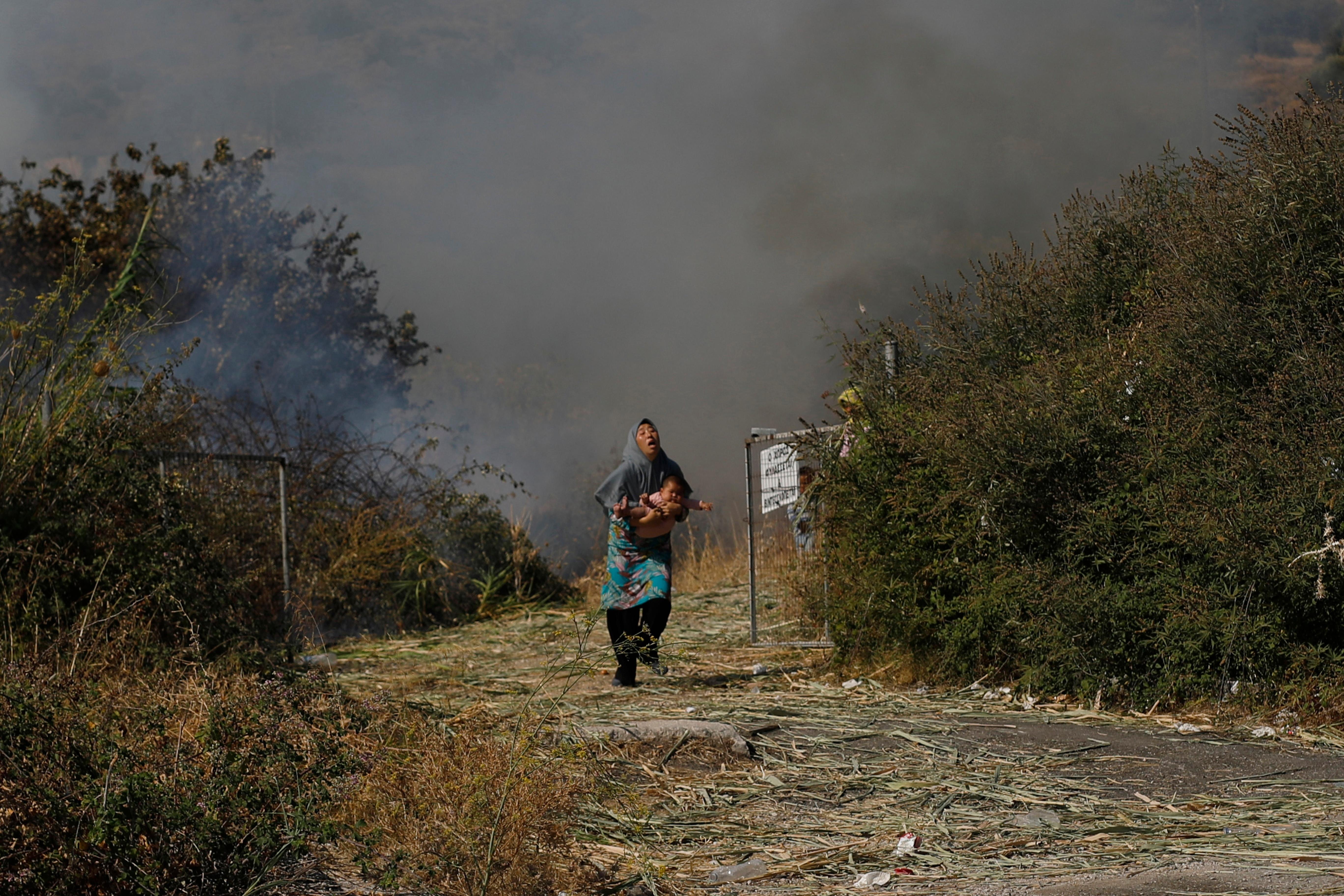 A migrant holds her baby as she runs to avoid a small fire in a field near Mytilene town, on the northeastern island of Lesbos, Greece, Saturday, Sept. 12, 2020. Greek authorities have been scrambling to find a way to house more than 12,000 people left in need of emergency shelter on the island after the fires deliberately set on Tuesday and Wednesday night gutted the Moria refugee camp. (AP Photo/Petros Giannakouris)