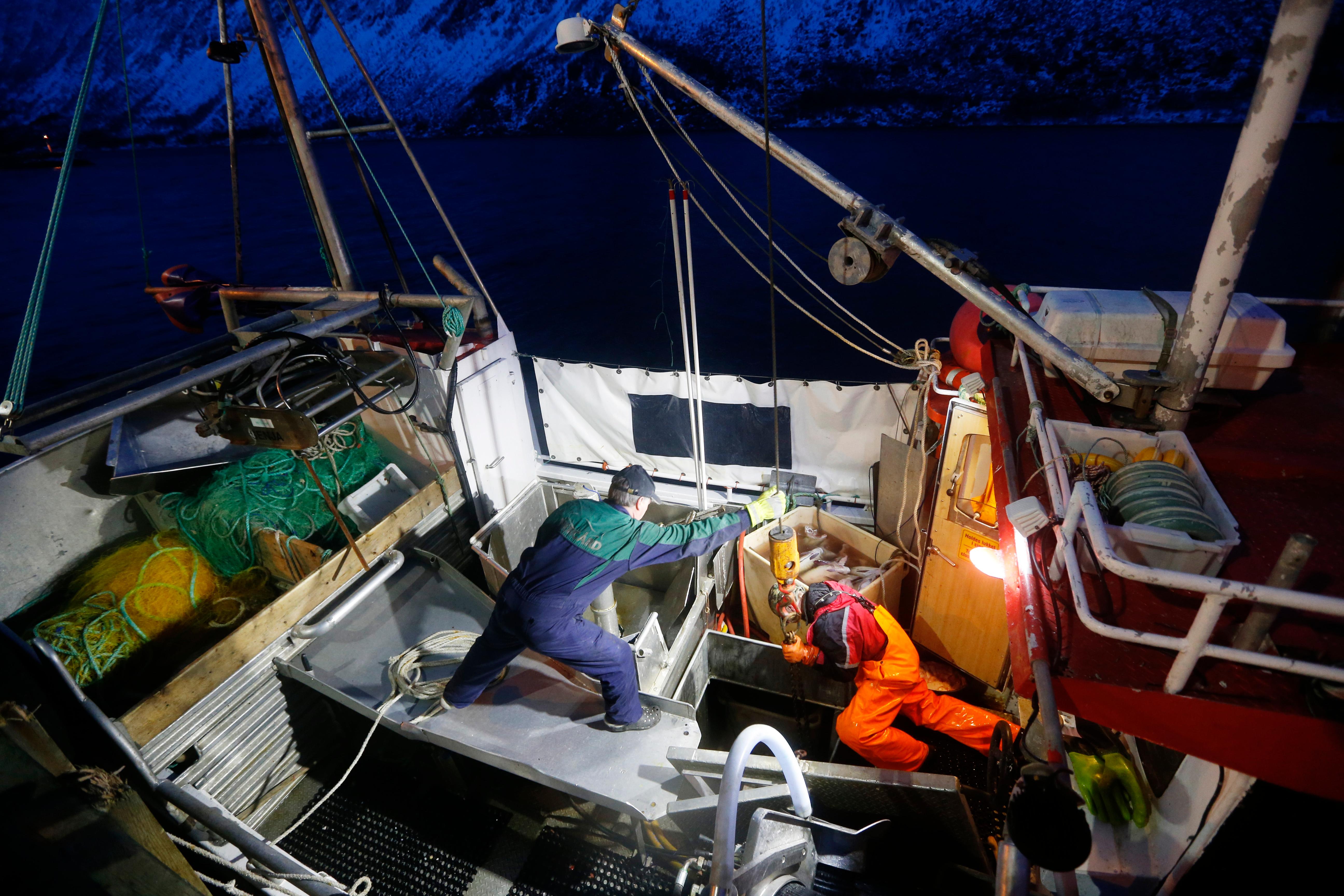 Bildet er fra en fiskebåt. Bildet er tatt høyt oppe, og ned mot to personer som jobber på dekk på båten.