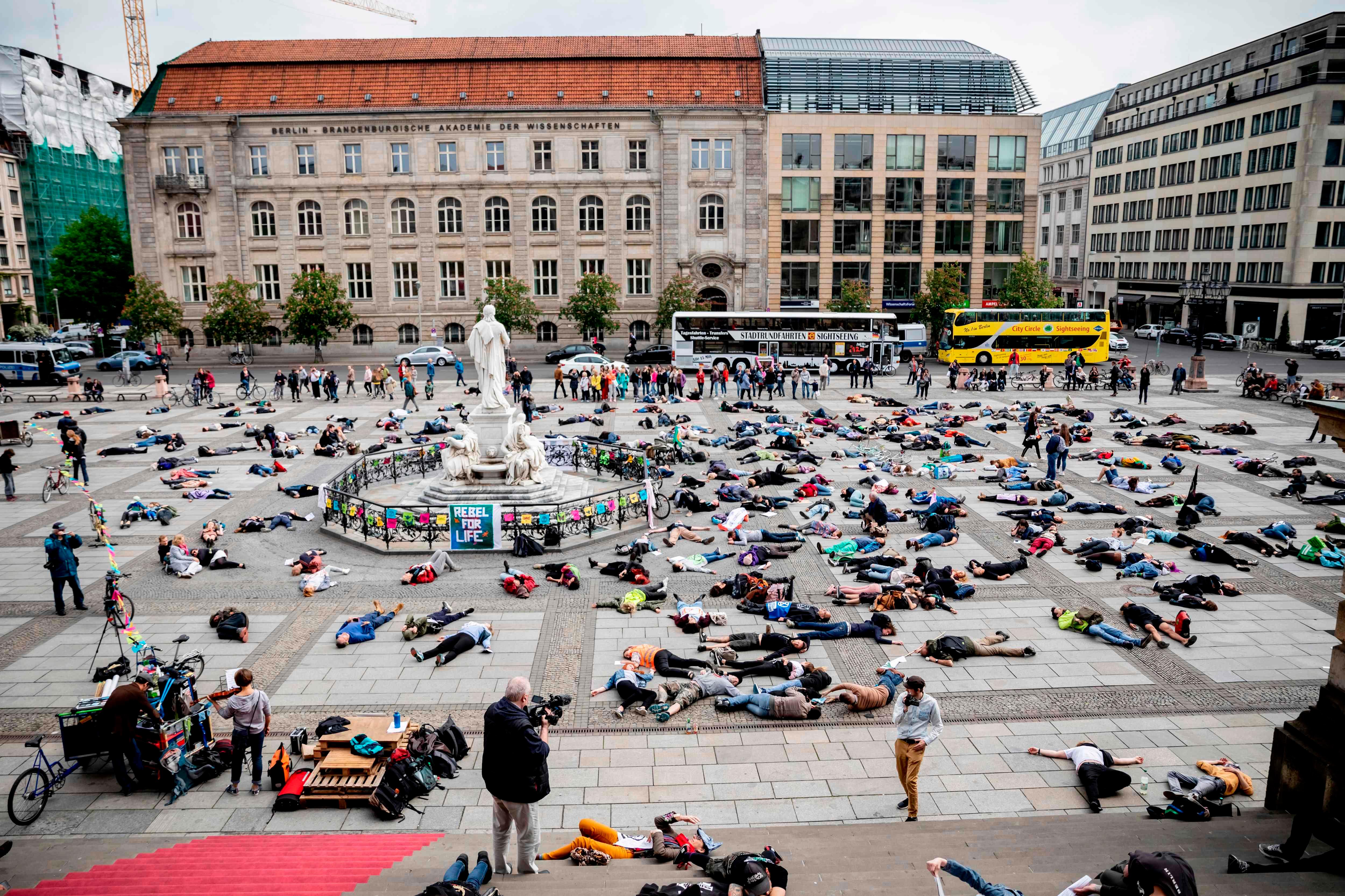 Extinction Rebellion (XR) climate change activists lie on the floor to symbolize a "mass die" at the Gendarmenmarkt square in Berlin on April 27, 2019. - Extinction Rebellion (XR) is an international movement that uses non-violent civil disobedience to achieve radical change in order to minimize the risk of human extinction and ecological collapse. (Photo by Christoph Soeder / dpa / AFP) / Germany OUT