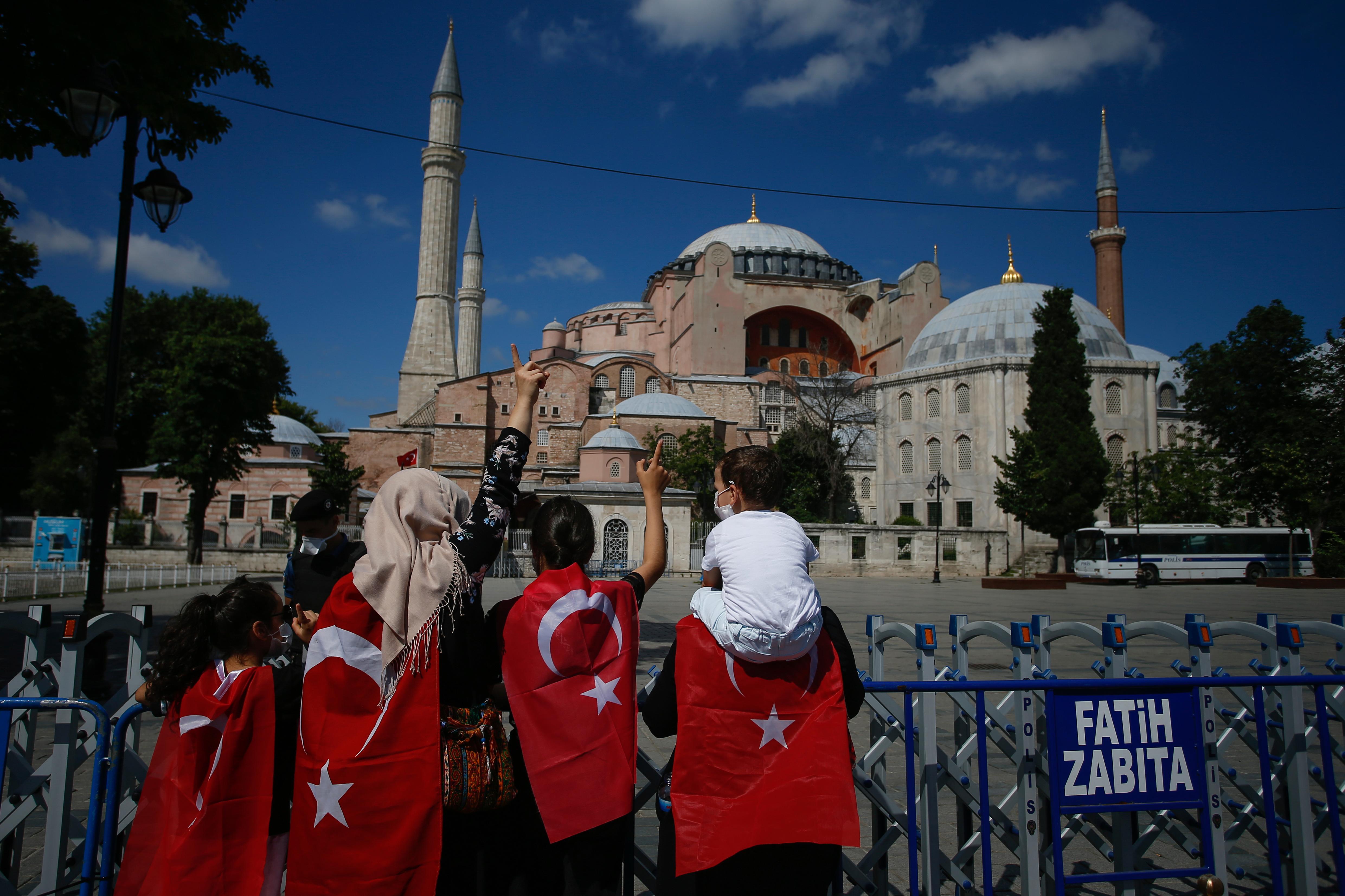 People, draped in Turkish flags stand outside the now closed Byzantine-era Hagia Sophia, one of Istanbul's main tourist attractions in the historic Sultanahmet district of Istanbul, Saturday, July 11, 2020. Turkey's President Recep Tayyip Erdogan formally reconverted Hagia Sophia into a mosque and declared it open for Muslim worship, hours after a high court annulled a 1934 decision that had made the religious landmark a museum.The decision sparked deep dismay among Orthodox Christians. Originally a cathedral, Hagia Sophia was turned into a mosque after Istanbul's conquest by the Ottoman Empire but had been a museum for the last 86 years, drawing millions of tourists annually. (AP Photo/Emrah Gurel)