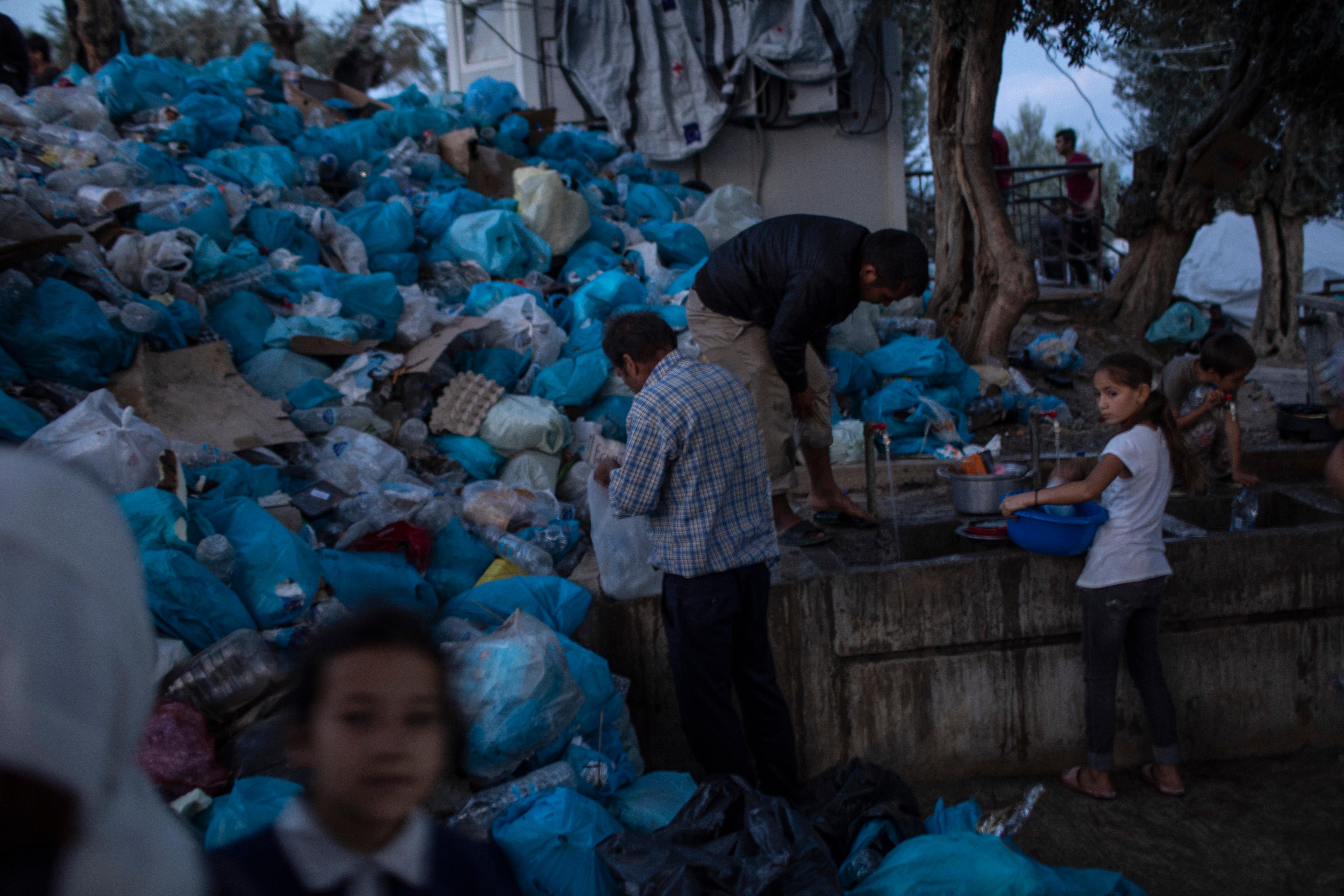 In this Thursday, Oct. 3, 2019 photo, people use the public wash area, in front of a pile of garbage bags at a makeshift refugee and migrant camp next to the overcrowded Moria camp on the Greek island of Lesbos. (AP Photo/Petros Giannakouris)