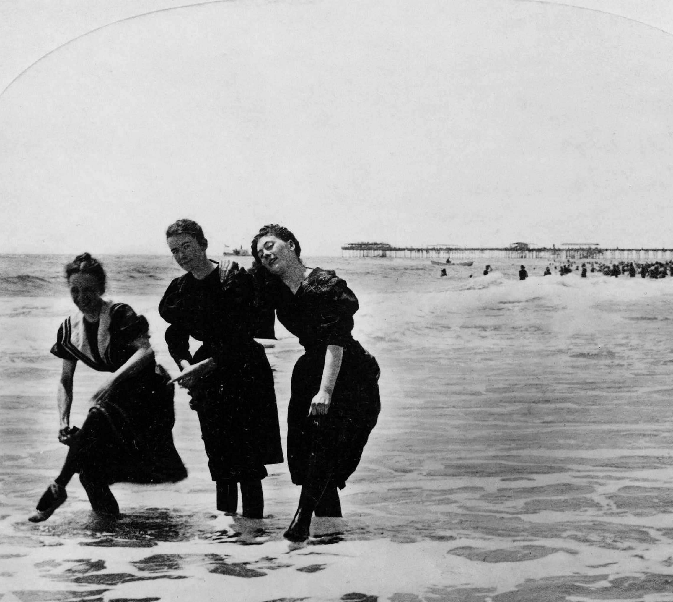 1890-1900: Kvinner på stranden i Atlantic City, New Jersey i 1897. Kvinnelig bademote speiler i stor grad moten ellers. I den grad bademoten utviklet sitt eget motevokabular, ble klærne ofte laget av ull eller flanell i mørke farger, og med detaljer som matroskrager og flettemønstre i kontrast-erende farger. Heldekkende mørke strømper dekket beina til på en sømmelig måte, og flate badesko, ofte med bånd krysset opp over anklene beskyttet føttene. FOTO: THE GRANGER COLLECTION/TT/NTB SCANPIX