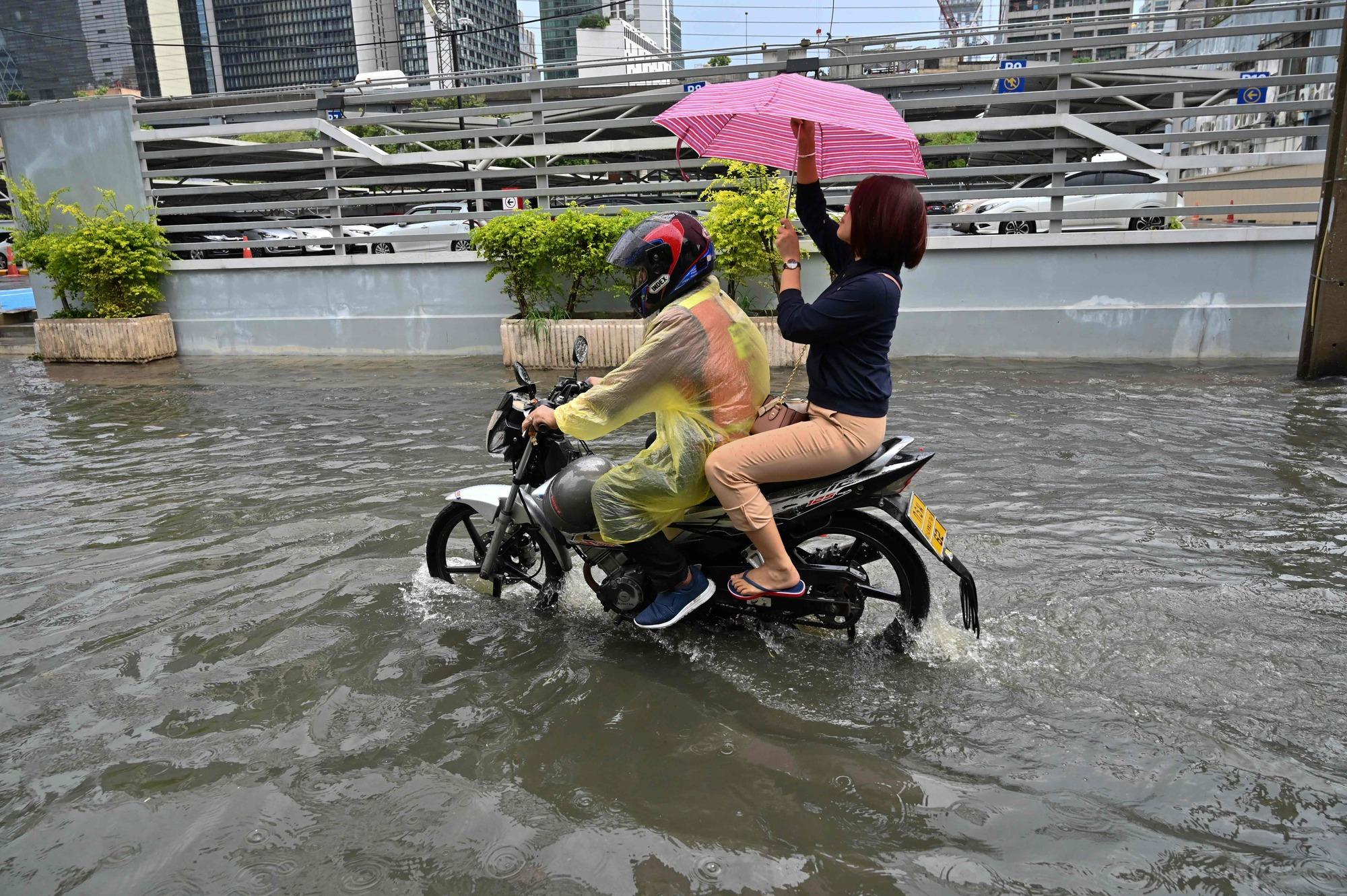 A woman adjusts her umbrella while riding a motorcycle taxi through a flooded street after heavy rain in Bangkok on June 7, 2019. (Photo by Romeo GACAD / AFP)