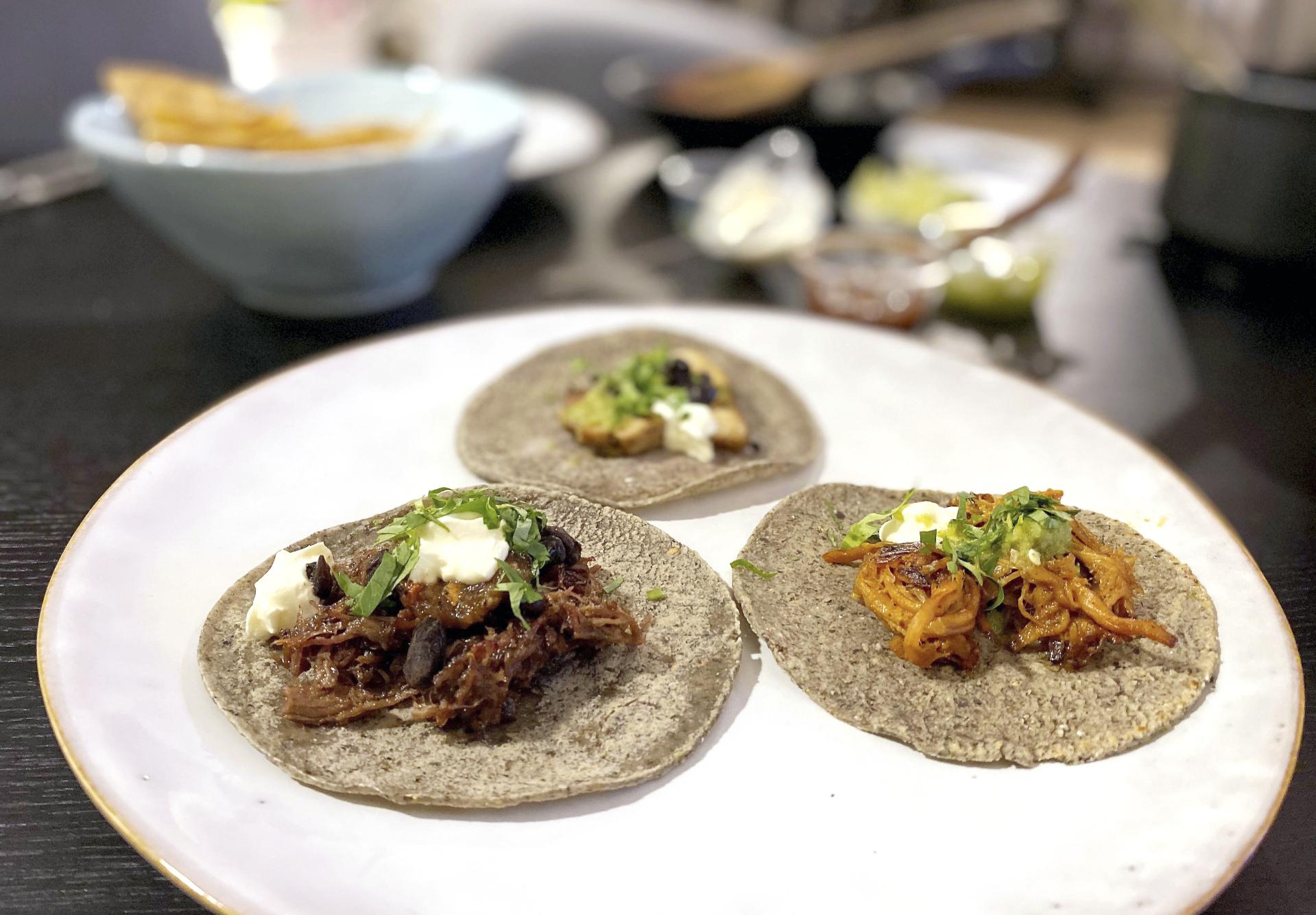 Til venstre ligger en tortilla med oksehale- og beinmargbarbacoa. Til høyre: cochinita pibil. Den bakerste retten er pollo al pastor.