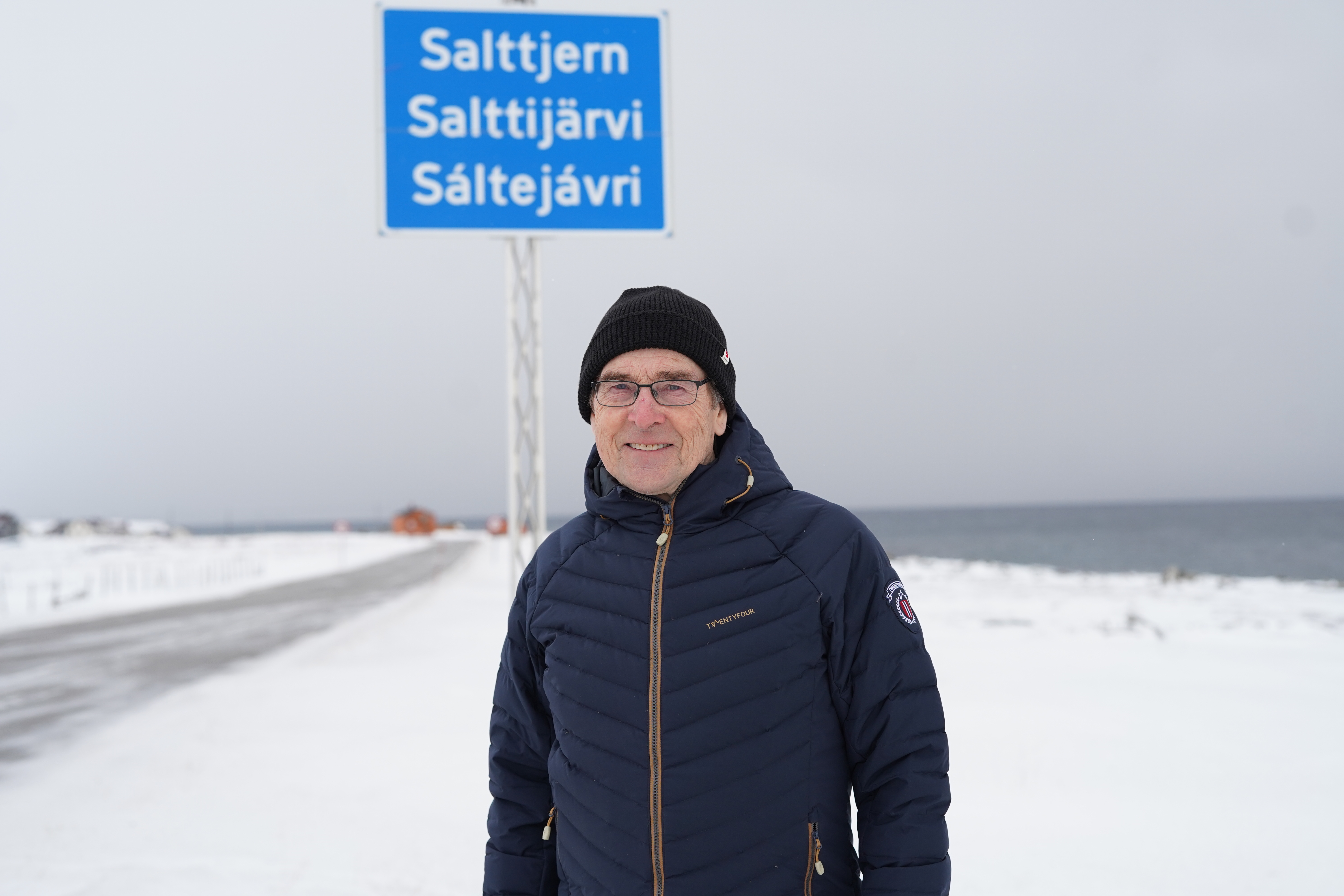 Einar Niemi foran skiltet der han bor i Varanger. Skiltet er på norsk, samisk og kvensk.