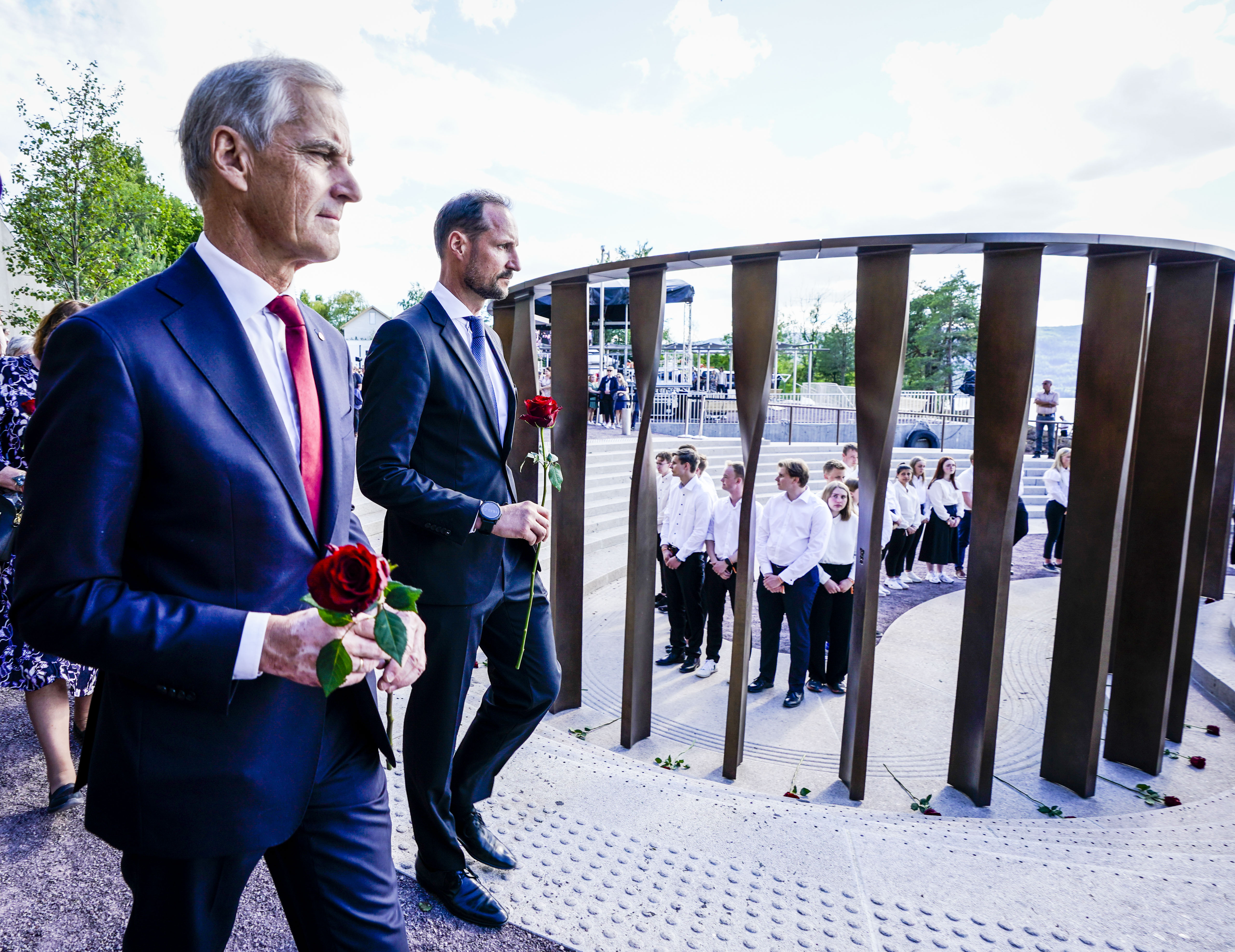 Jonas Gahr Støre og kronprins Håkon holder en rose hver. Bak dem ser vi de 77 søylene i bronse som er for å minne de som døde 22. juli.