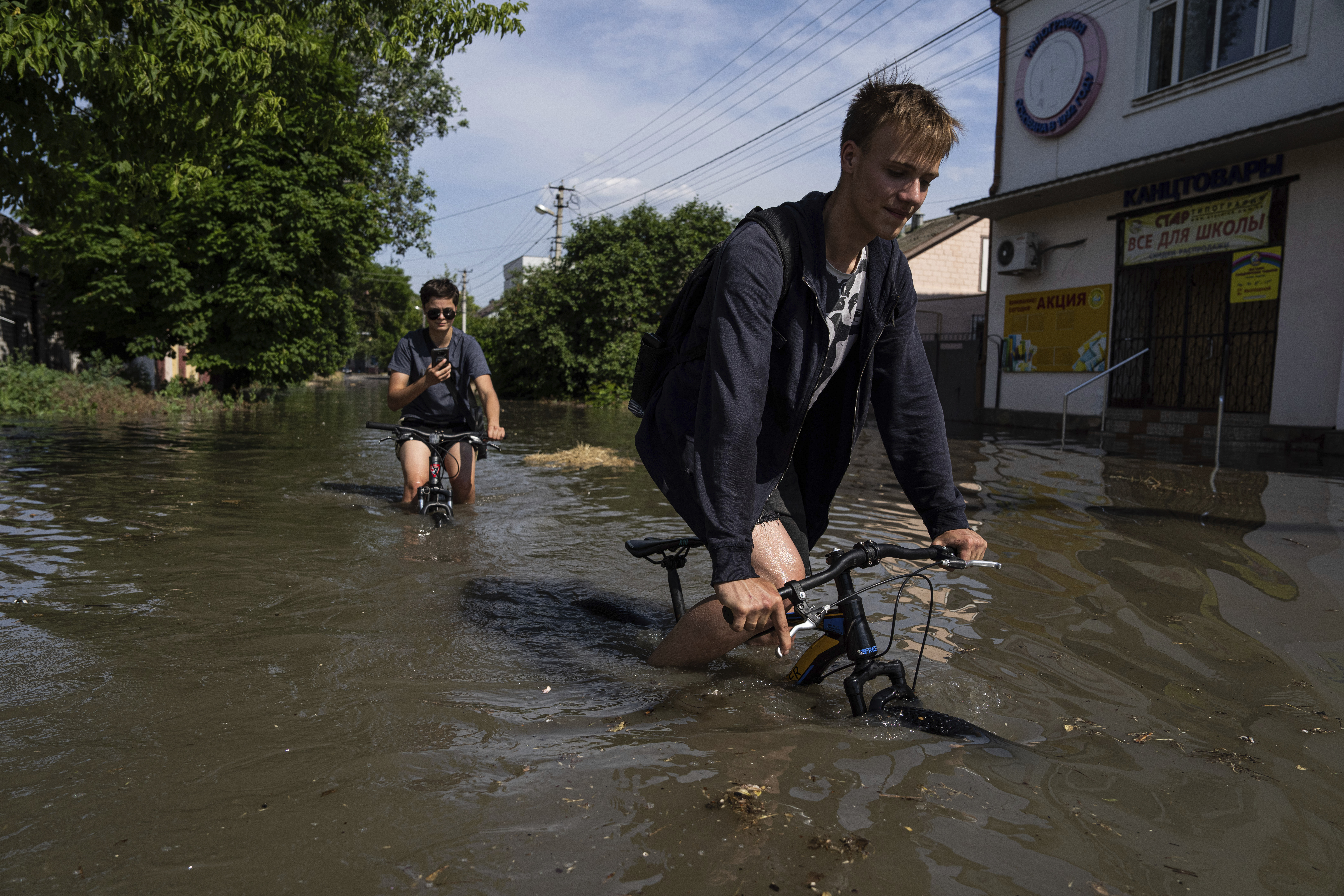 To gutter forsøker å sykle gjennom de store vannmassene i en landsby i Kherson-fylket tirsdag. Foto: Jevhen Maloletka / AP / NTB