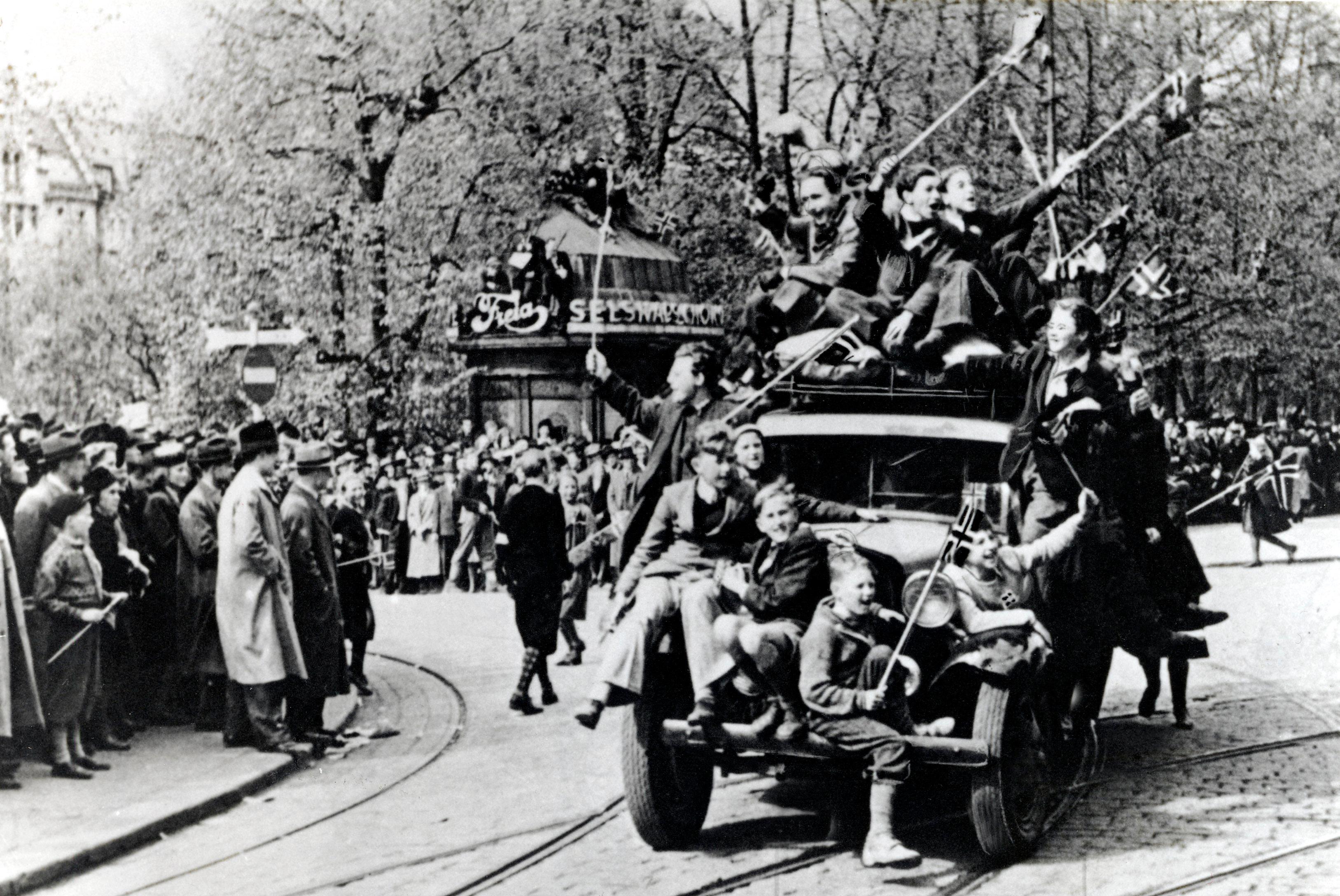 Oslo 19450508:  Fredsdagene mai 1945. Frigjøringsdagen 8. mai, jubel på Karl Johans gate. Biler fulle av jublende mennesker med norske flagg, folkemengder i gatene.
Foto: NTB / Scanpix