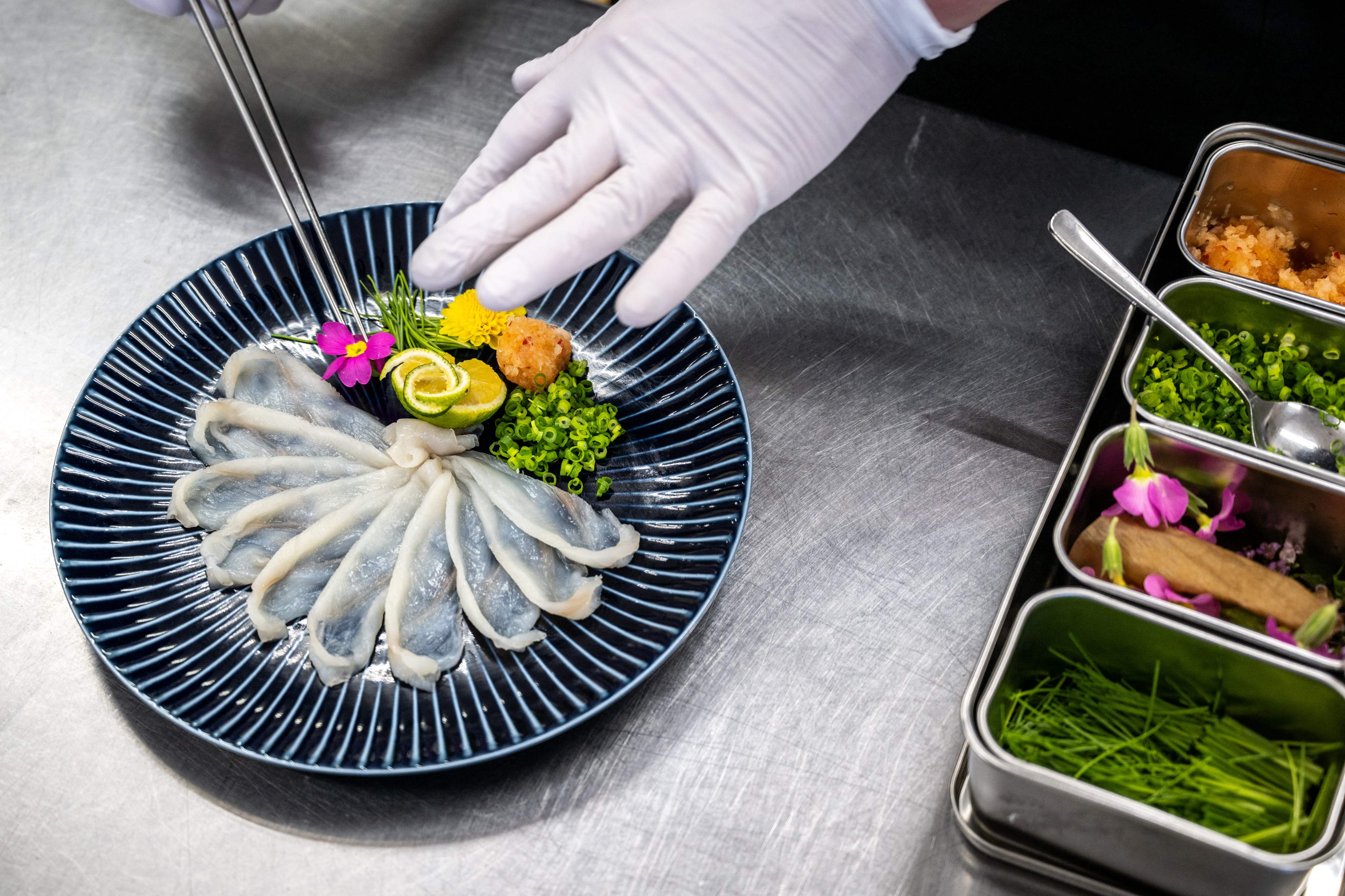 This photo taken on January 19, 2023 shows Yoshimasa Kanno, operator of the Minatoya hotel, handling slices of tiger puffer fish sashimi at his hotel in Soma city of Japan's Fukushima Prefecture. - The pufferfish filling fishermen's nets in Fukushima are a delicacy that can kill if wrongly prepared. To a community devastated by a 2011 nuclear disaster, however, they are also a lifeline. (Photo by Philip FONG / AFP) / To go with AFP story "Japan-nuclear-environment-fishing-Fukushima", FOCUS by Harumi OZAWA