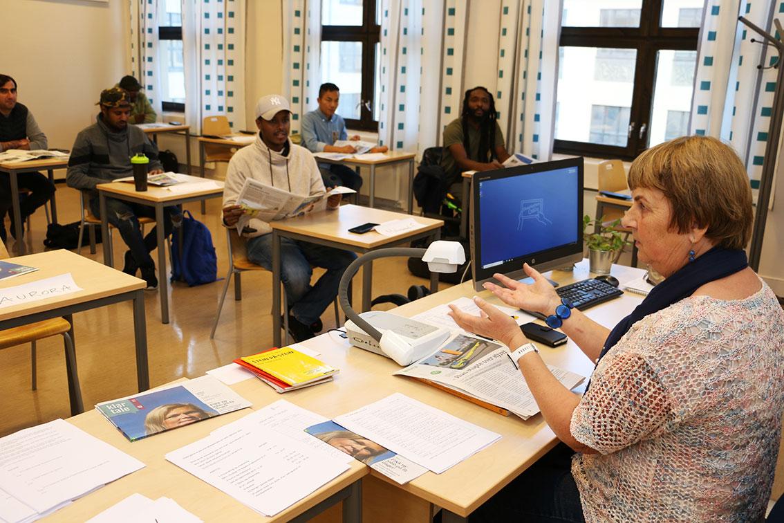 Bildet viser Bodil Johanne Knutsen bak kateteret i klasserommet på Rosenhof i Oslo. Foran henne sitter flere elever. Hun har undervist innvandrere i norsk i mange år. Hun bruker Klar Tale i undervisningen.