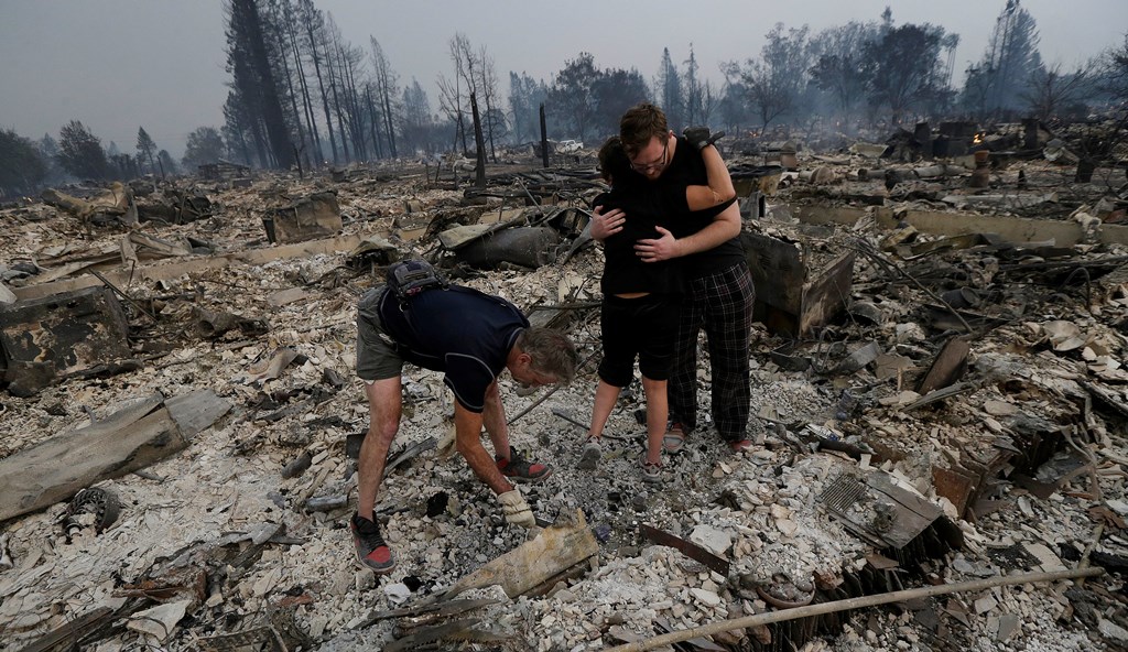 Michael Pond (t.v.) gjennomsøker ruinene av familiens hjem i Santa Rosa i California, mens kona Kristine får en klem fra datterens kjæreste Zack Thurston.