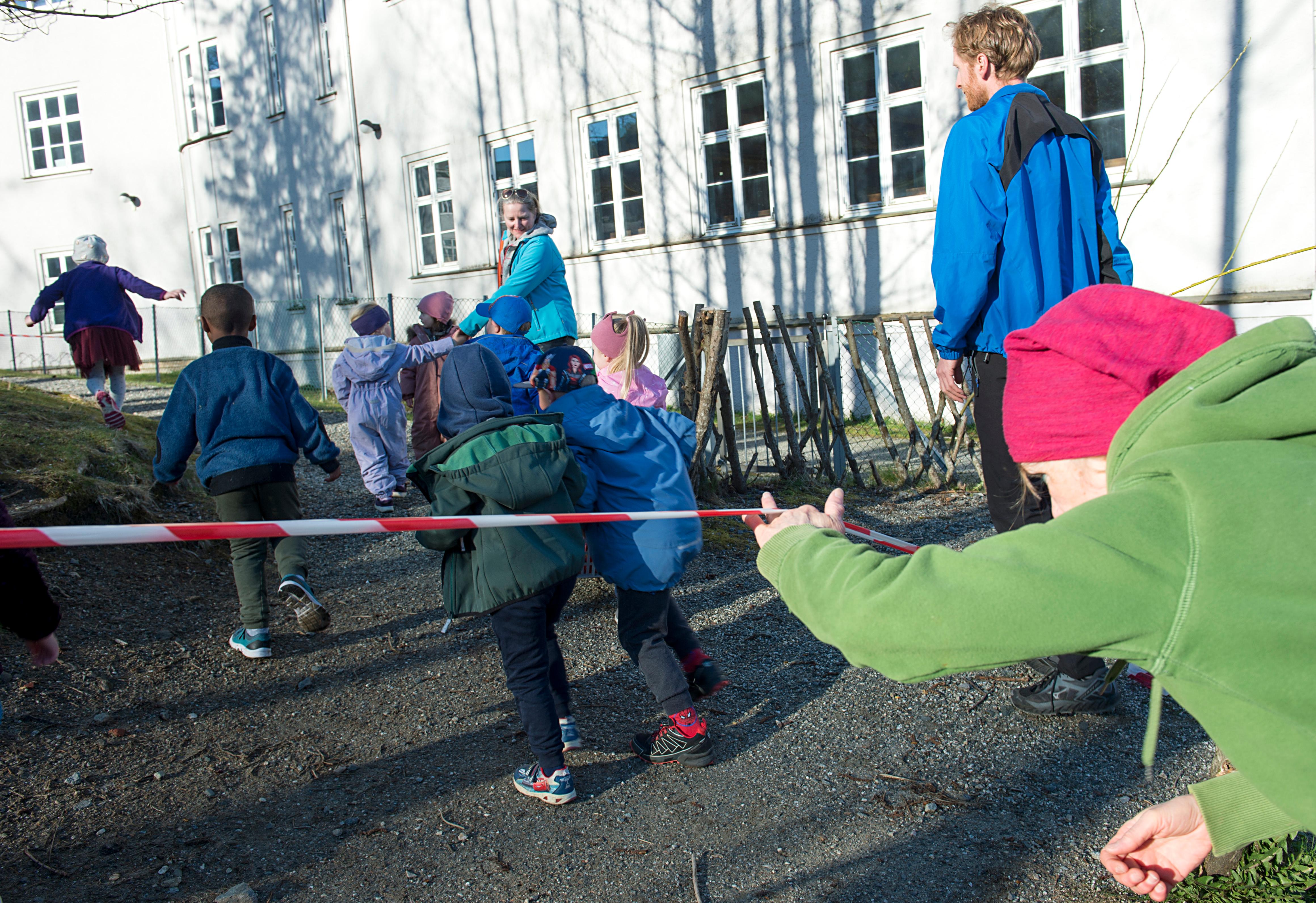 Bergen 20200420. 
 Barna løper under sperrebåndene mot inngangen til Årstad Brannstasjon barnehage etter  gjenåpningen mandag morgen. De ulike  gruppene med barn skal ha faste plasser  som er avsperret når de er ute og leker.
Foto: Marit Hommedal / NTB scanpix