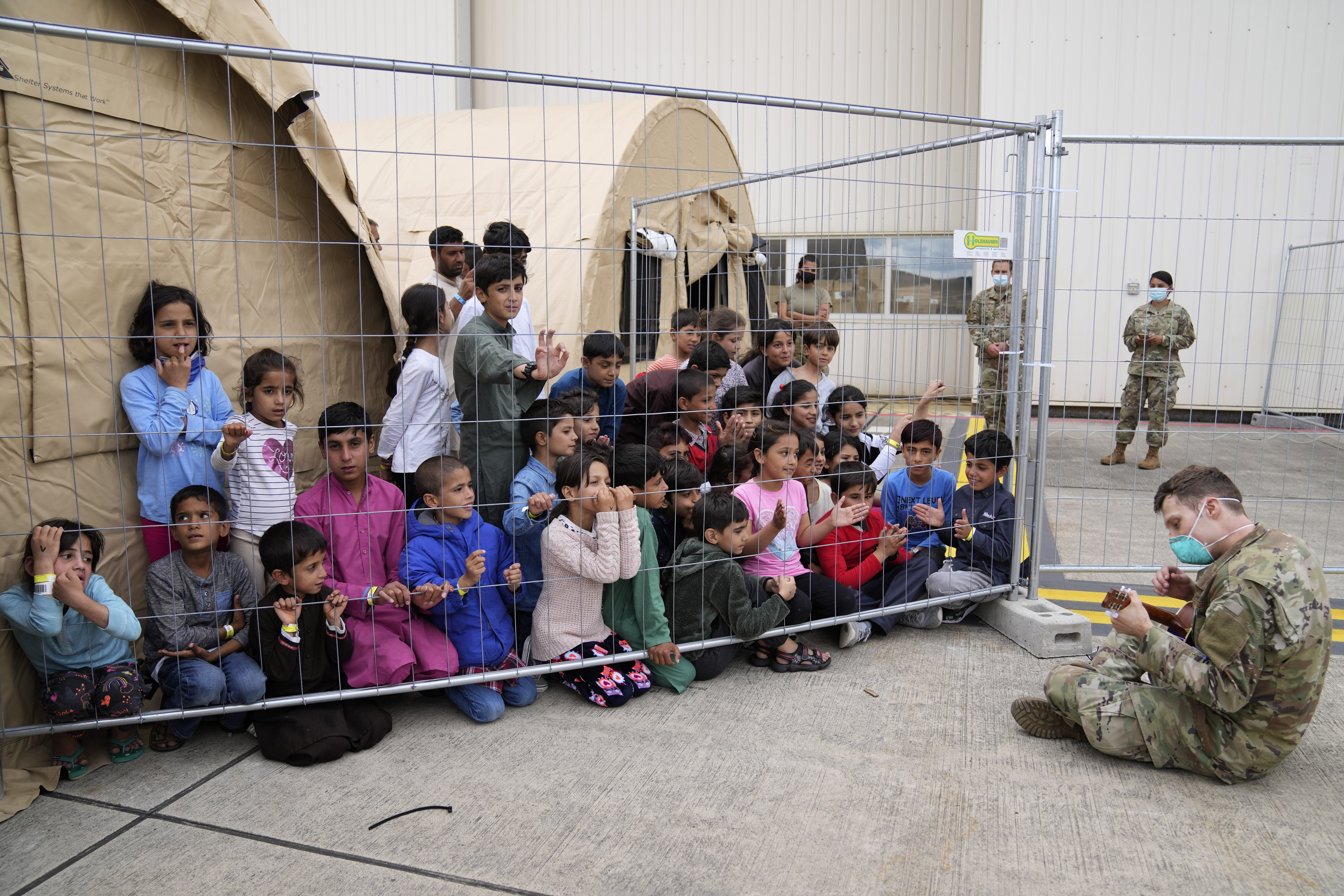 An U.S. soldier plays guitar for recently evacuated Afghan children at the Ramstein U.S. Air Base, Germany, Tuesday, Aug. 24, 2021. (AP Photo/Matthias Schrader)