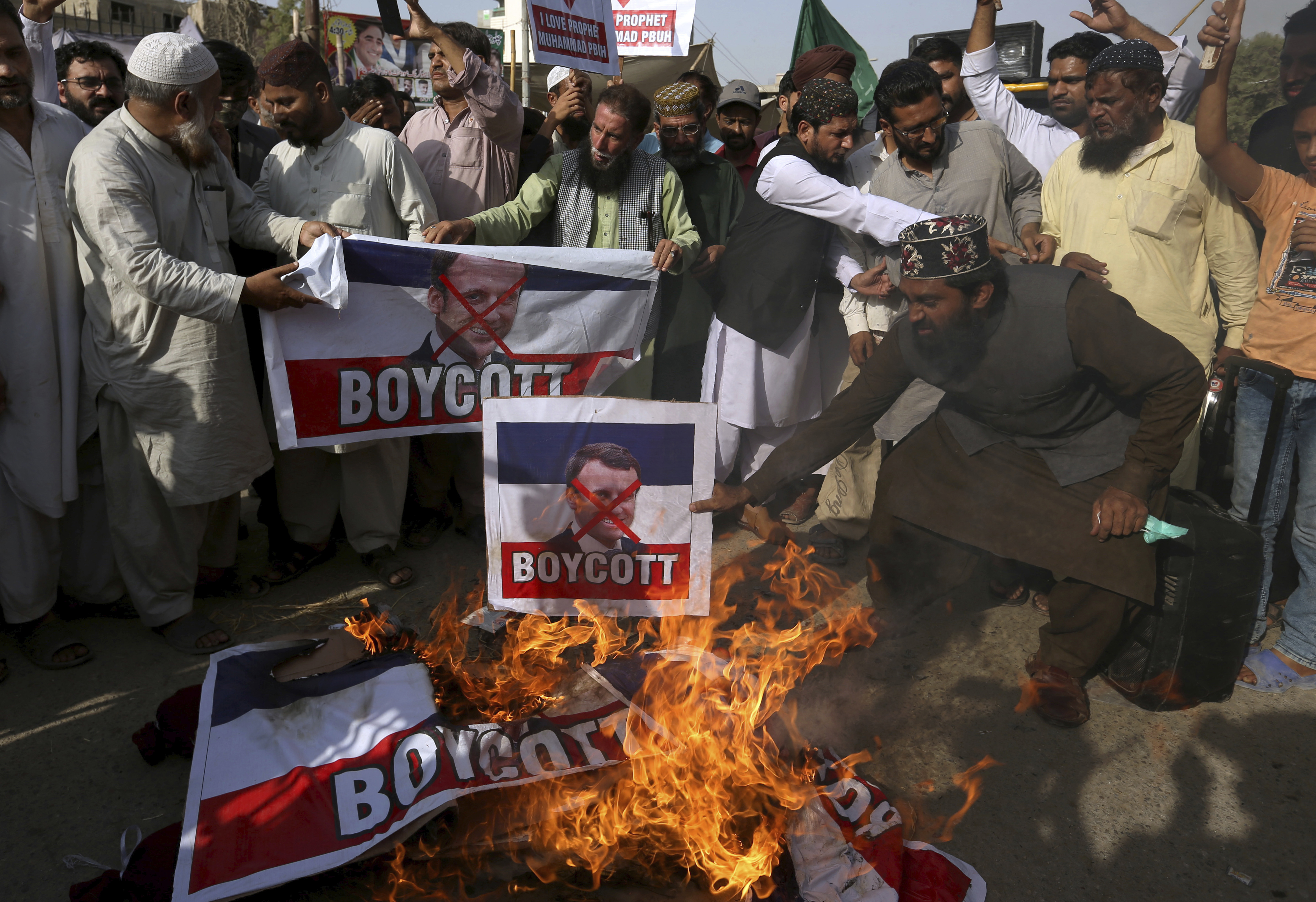 Supporters of the religious group, "Tahaful-e-Islam Pakistan," burn representations of the French flags with defaced images of French President Emmanuel Macron during a protest against the publishing of caricatures of the Muslim Prophet Muhammad they deem blasphemous, in Karachi, Pakistan, Tuesday, Oct. 27, 2020. (AP Photo/Fareed Khan)