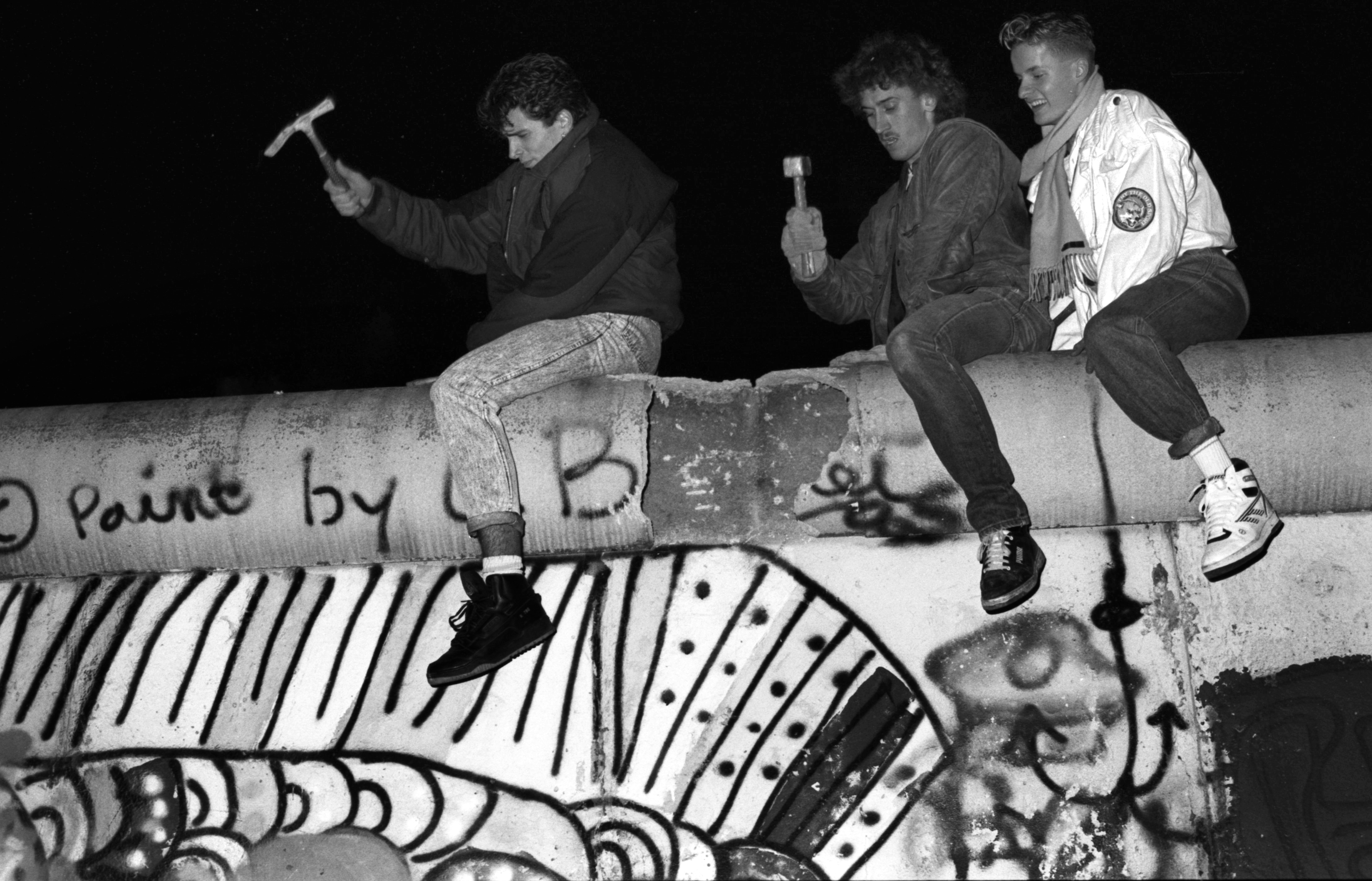 Tres jóvenes, dos de ellos con un martillo y un pico, golpean el Muro de Berlín durante su caída, en la República Democrática de Alemania.