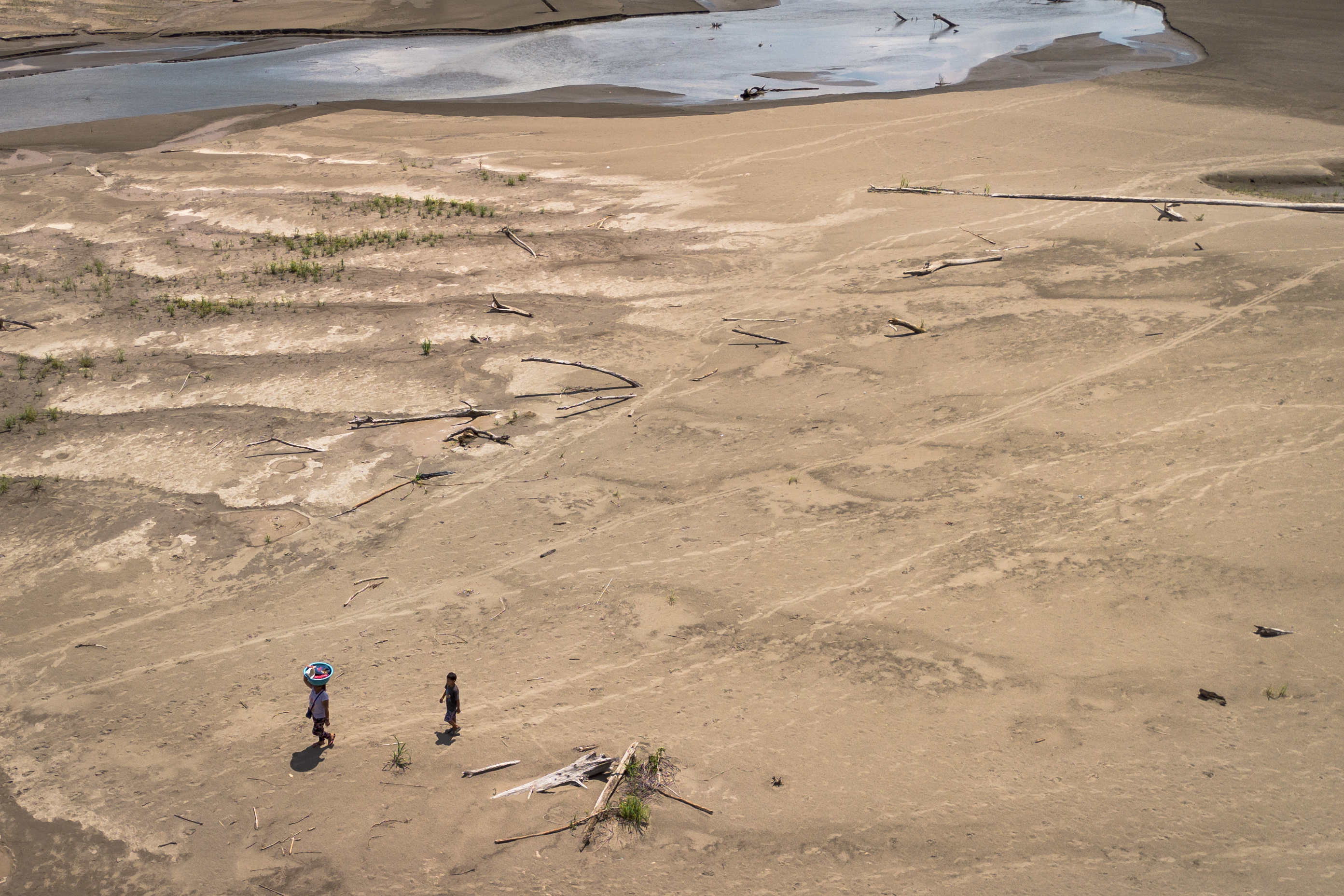 Artea Pérez y su hijo caminan bajo el sol por una playa seca de regreso a su comunidad, el 16 de octubre de 2024.