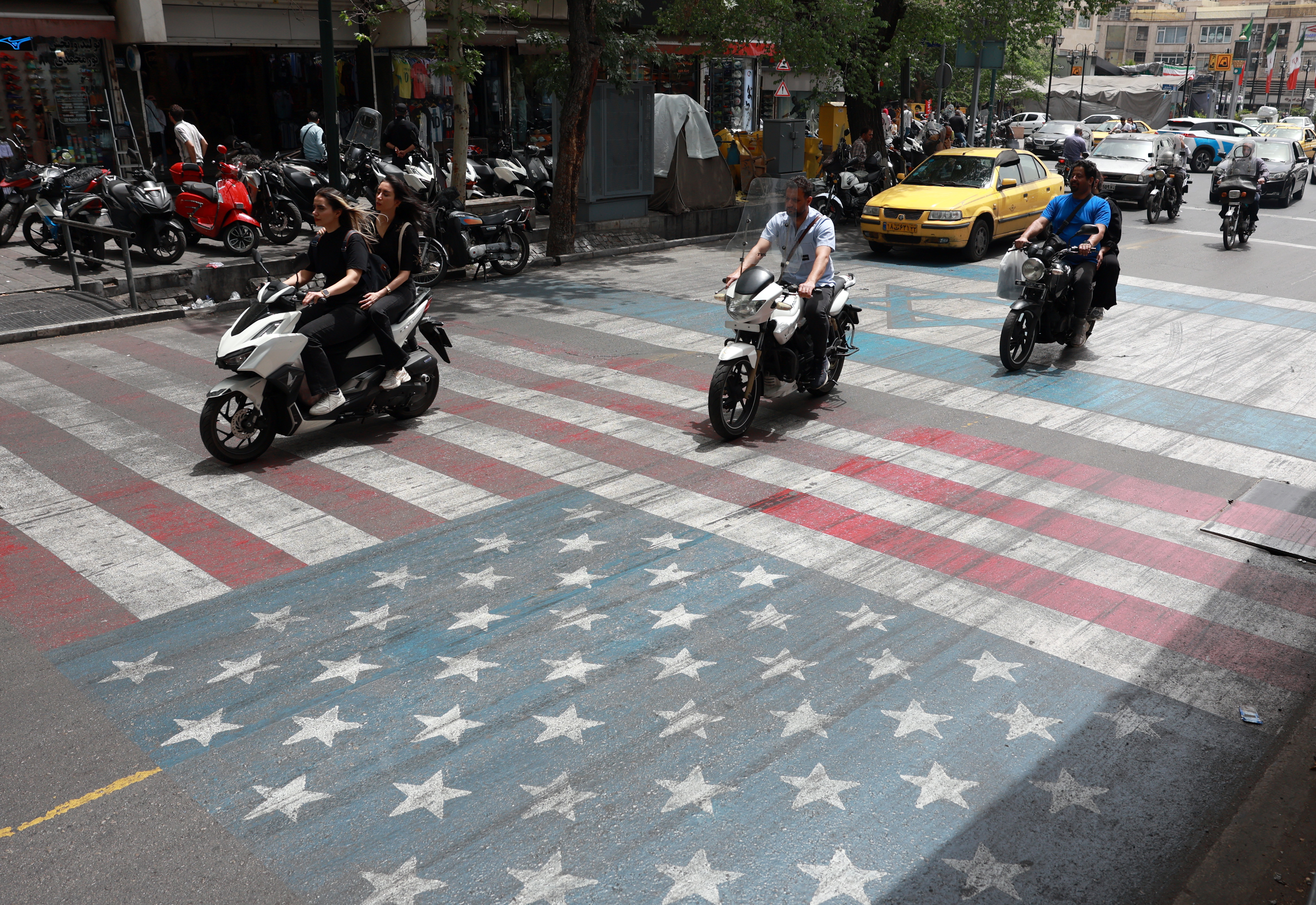 Ciudadanos iraníes manejan sobre una pintada de la bandera de Estados Unidos, en el centro de Teherán, Irán, este lunes 4 de abril.
