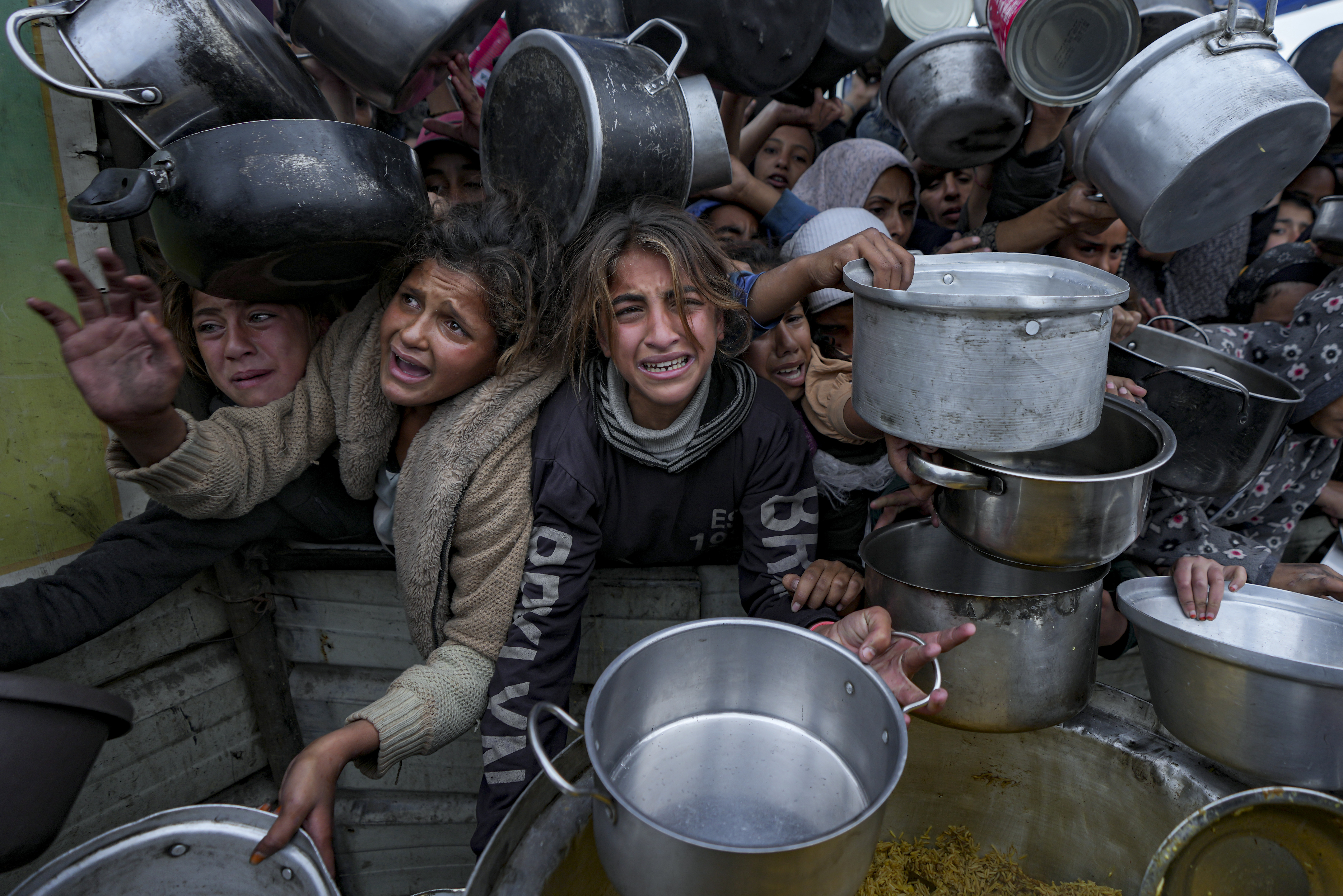 Palestinian women and girls struggle to reach for food at a distribution center in Khan Younis, Gaza Strip, Friday, Dec. 20, 2024. (AP Photo/Abdel Kareem Hana)