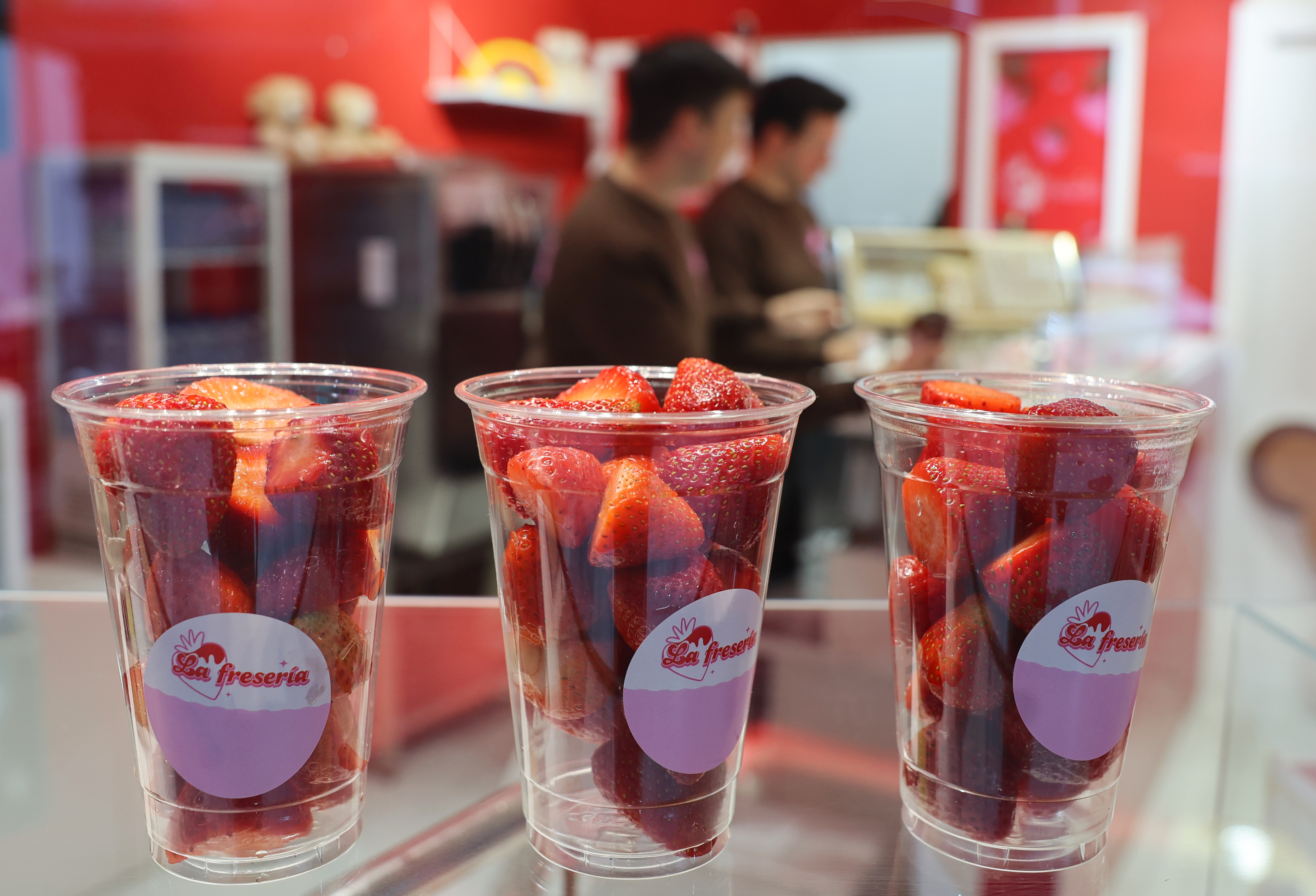 Vaso de fresones cortados con salsa de chocolate y toppings en un mostrador de local urbano