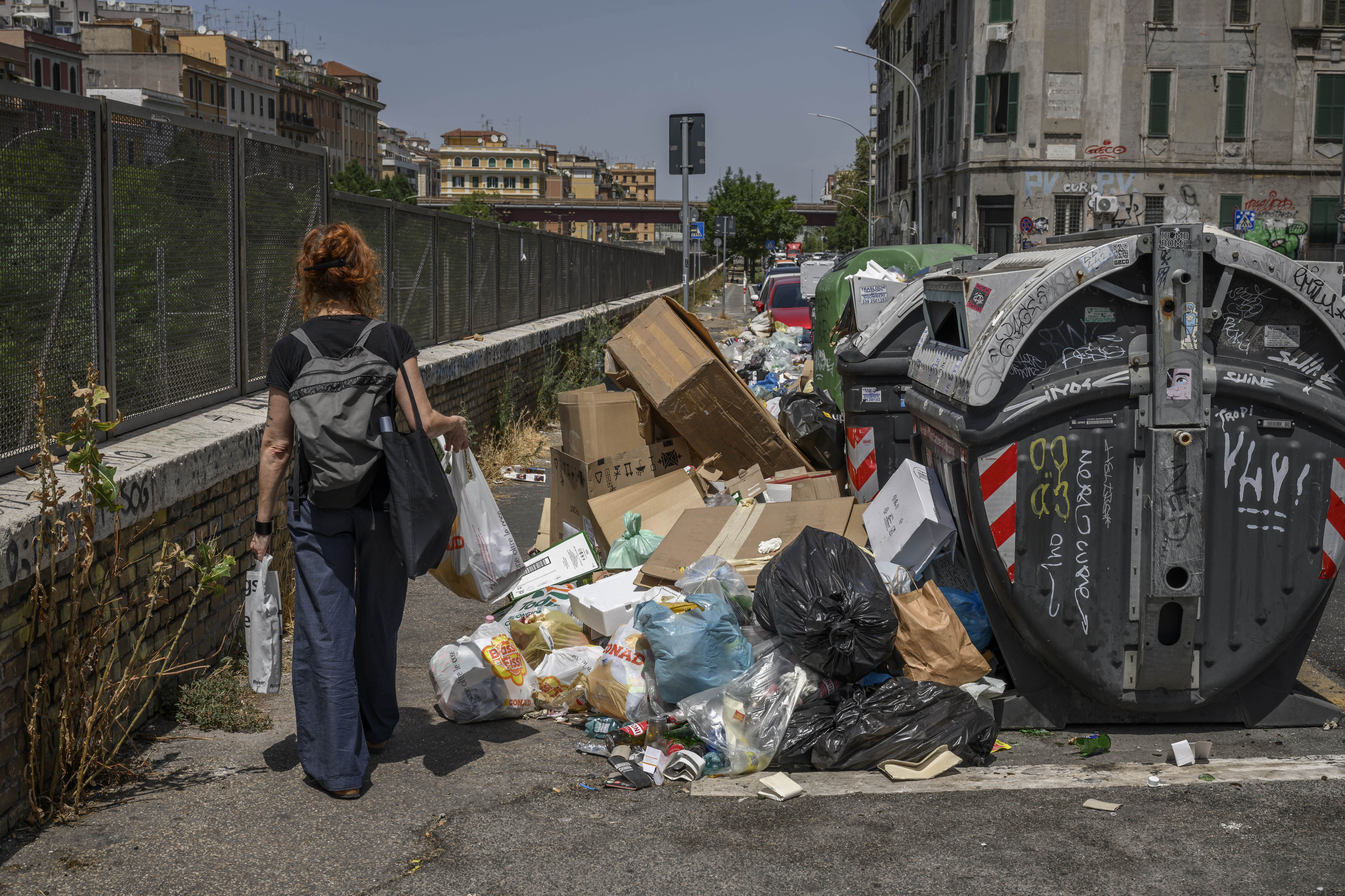 Uma mulher passa por latas de lixo transbordando no bairro de Pigneto, em Roma, em 21 de julho.