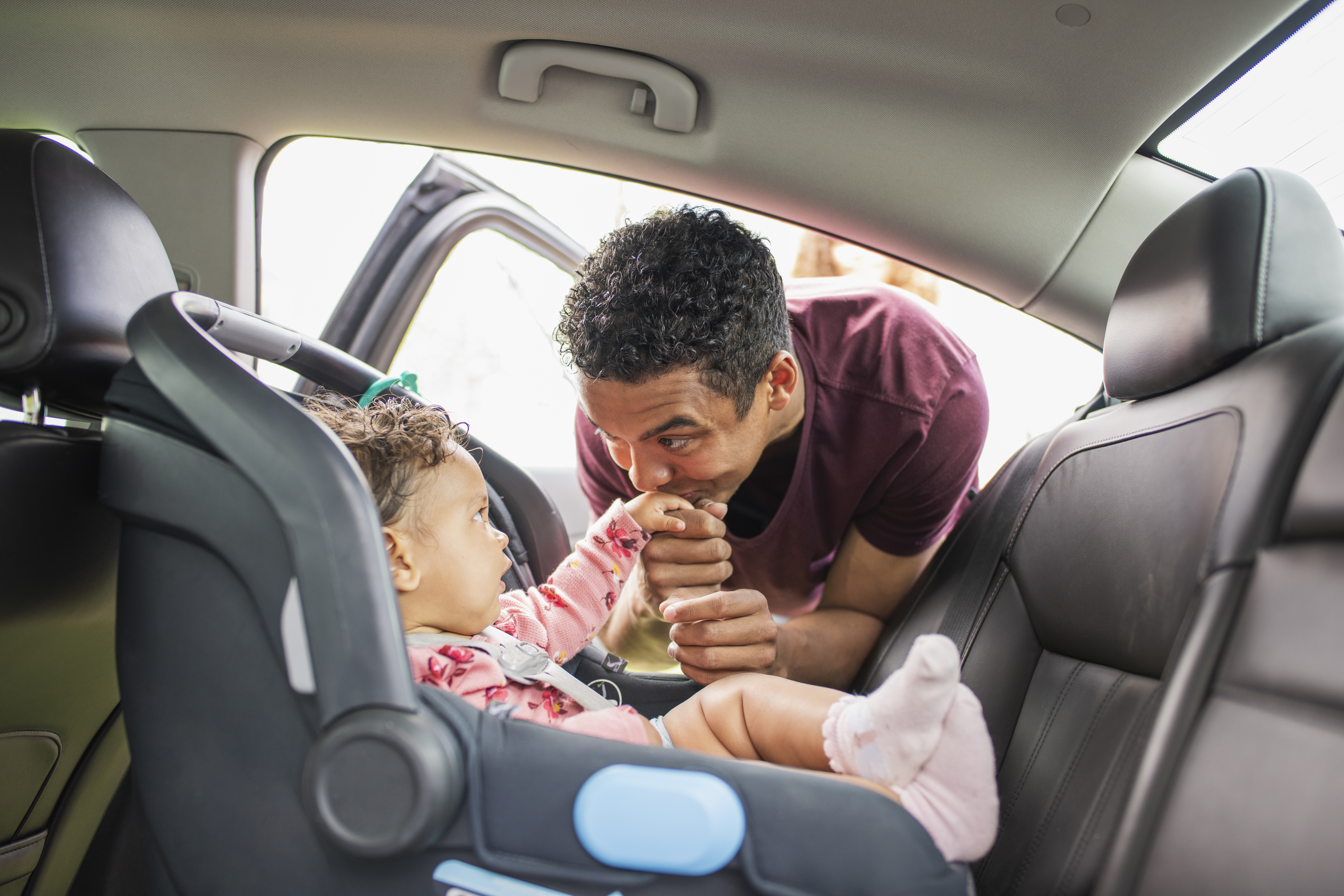 Padre joven poniendo a la niña en el asiento del coche.