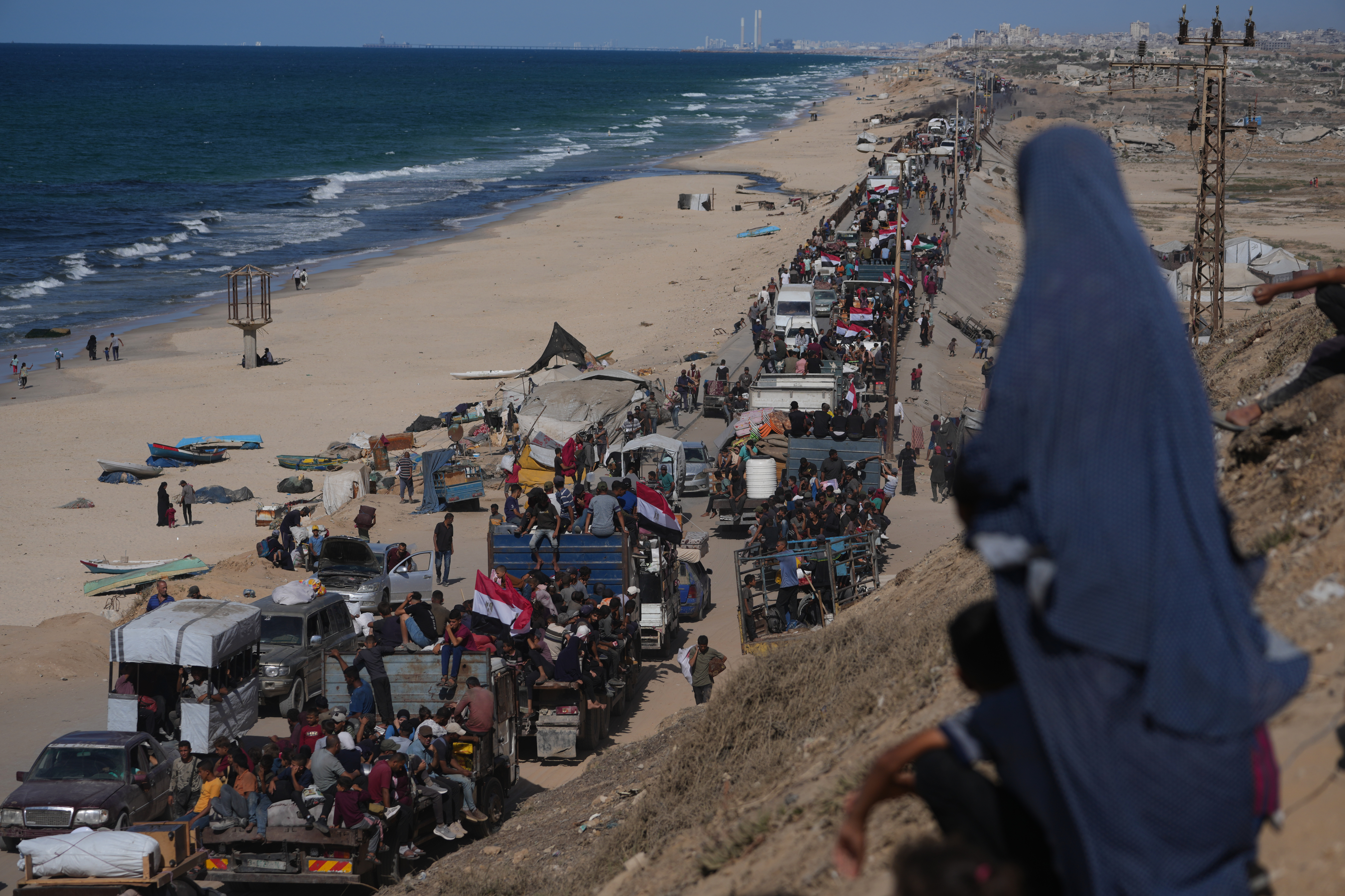 Displaced Palestinians ride on trucks loaded with belongings and wave Egyptian and Palestinian flags as they travel along the coastal road near Wadi Gaza in the central Gaza Strip, moving toward Gaza city, Saturday, Oct. 11, 2025, after Israel and Hamas agreed to a pause in their war and the release of the remaining hostages. (AP Photo/Jehad Alshrafi)