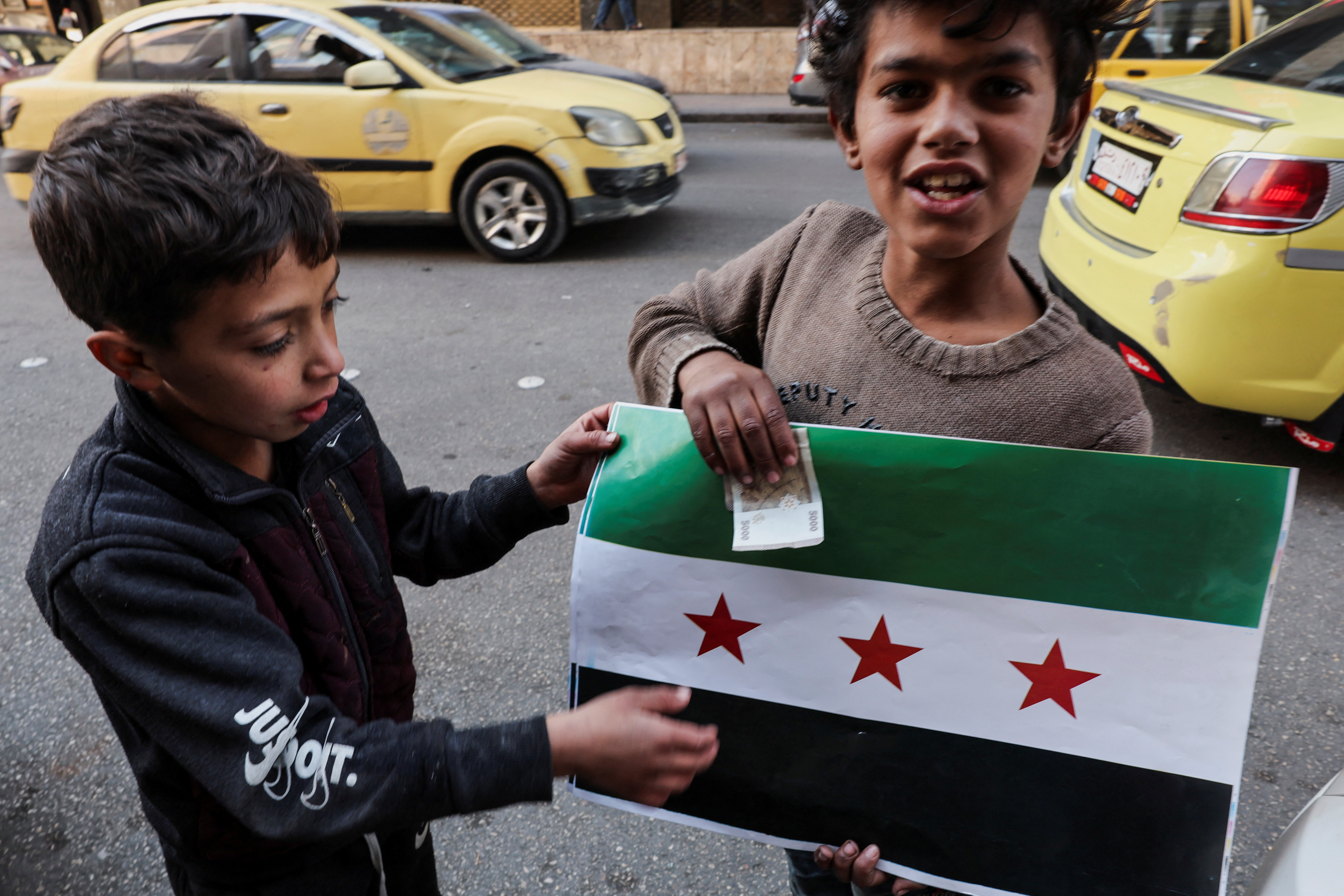 A boy sells pictures of the flag adopted by the new Syrian rulers, after the ousting of Syria's Bashar al-Assad, in Damascus, Syria, December 16, 2024. REUTERS/Amr Abdallah Dalsh   