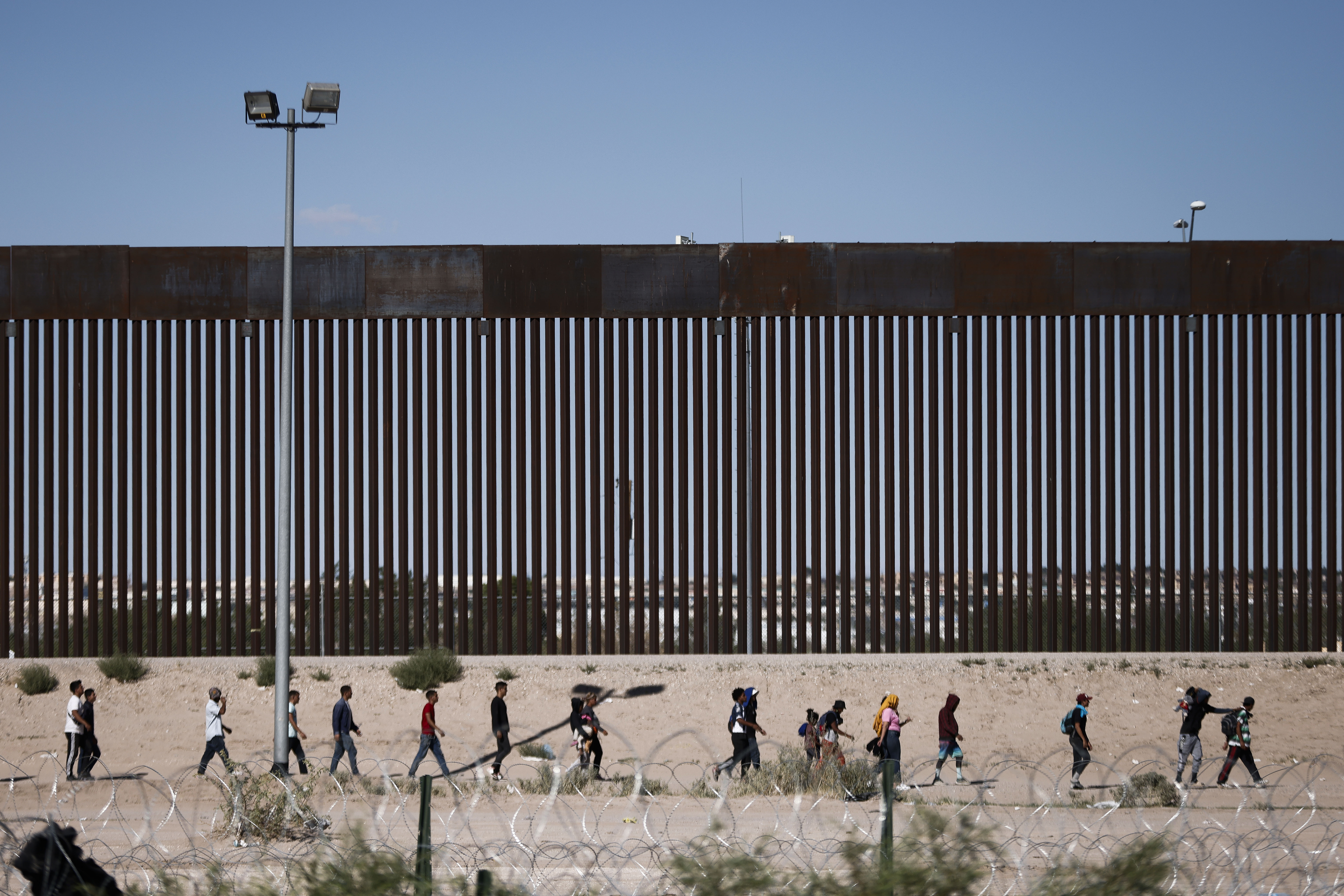 Un grupo de personas camina frente al muro fronterizo entre Ciudad Juárez (Chihuahua) y El Paso (Texas).