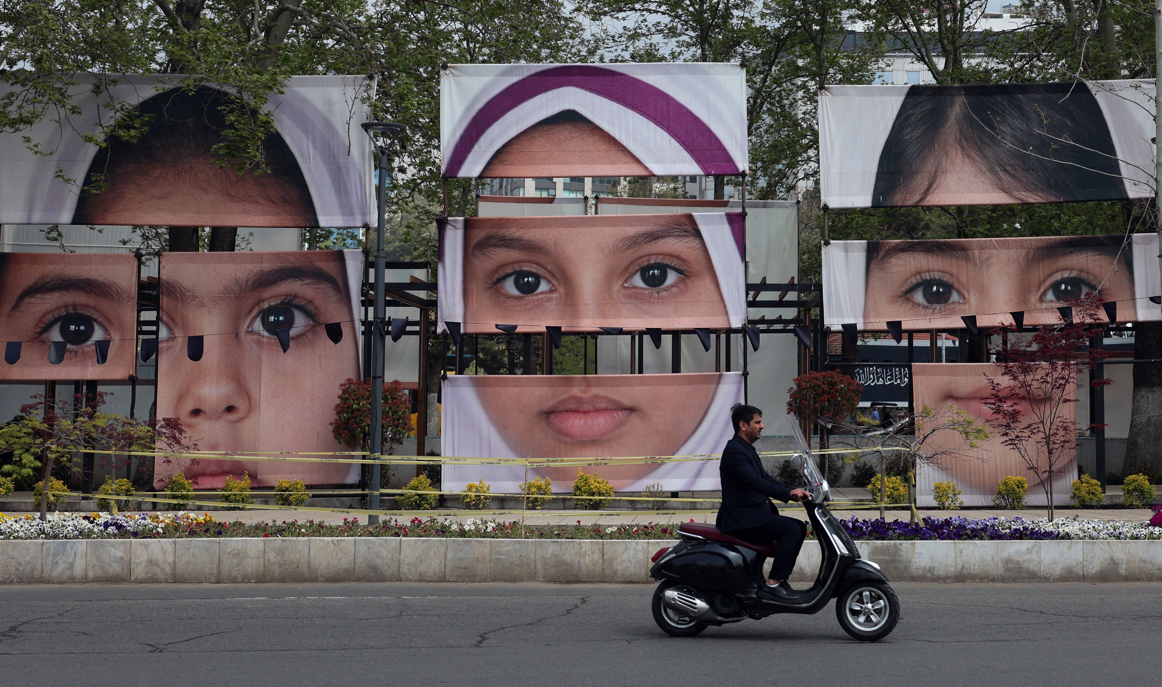 Una persona conduce una moto frente a carteles con los rostros de las menores iraníes asesinadas en un ataque en Teherán