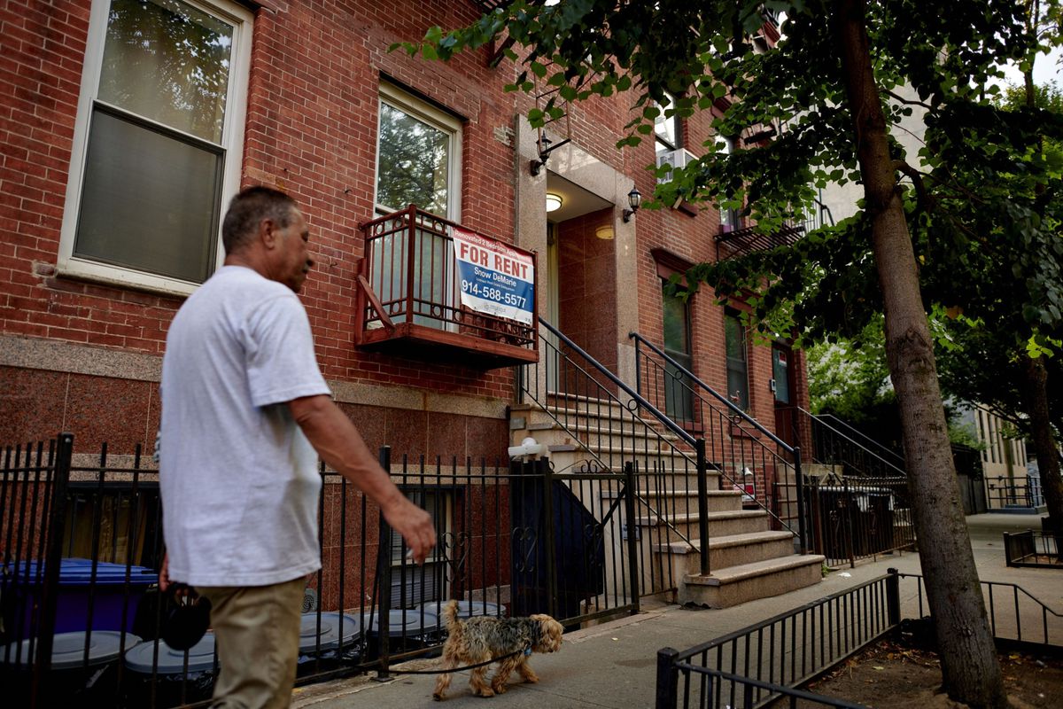 Un hombre pasea a su perro en el East Village de Nueva York junto a un cartel de se alquila piso.