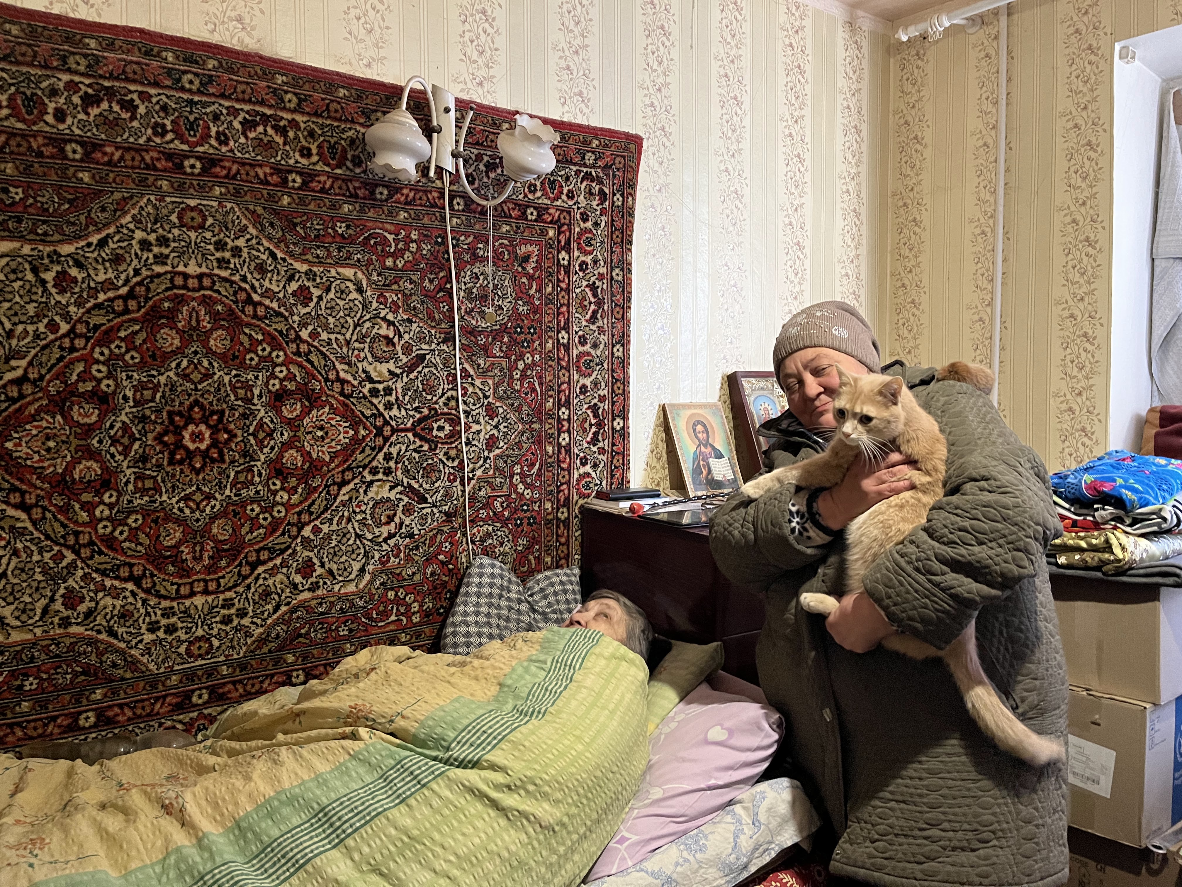 Liudmila, uma enfermeira aposentada de 79 anos, acamada no apartamento onde mora com Natacha, de pé com seu gato nos braços, em Limán.