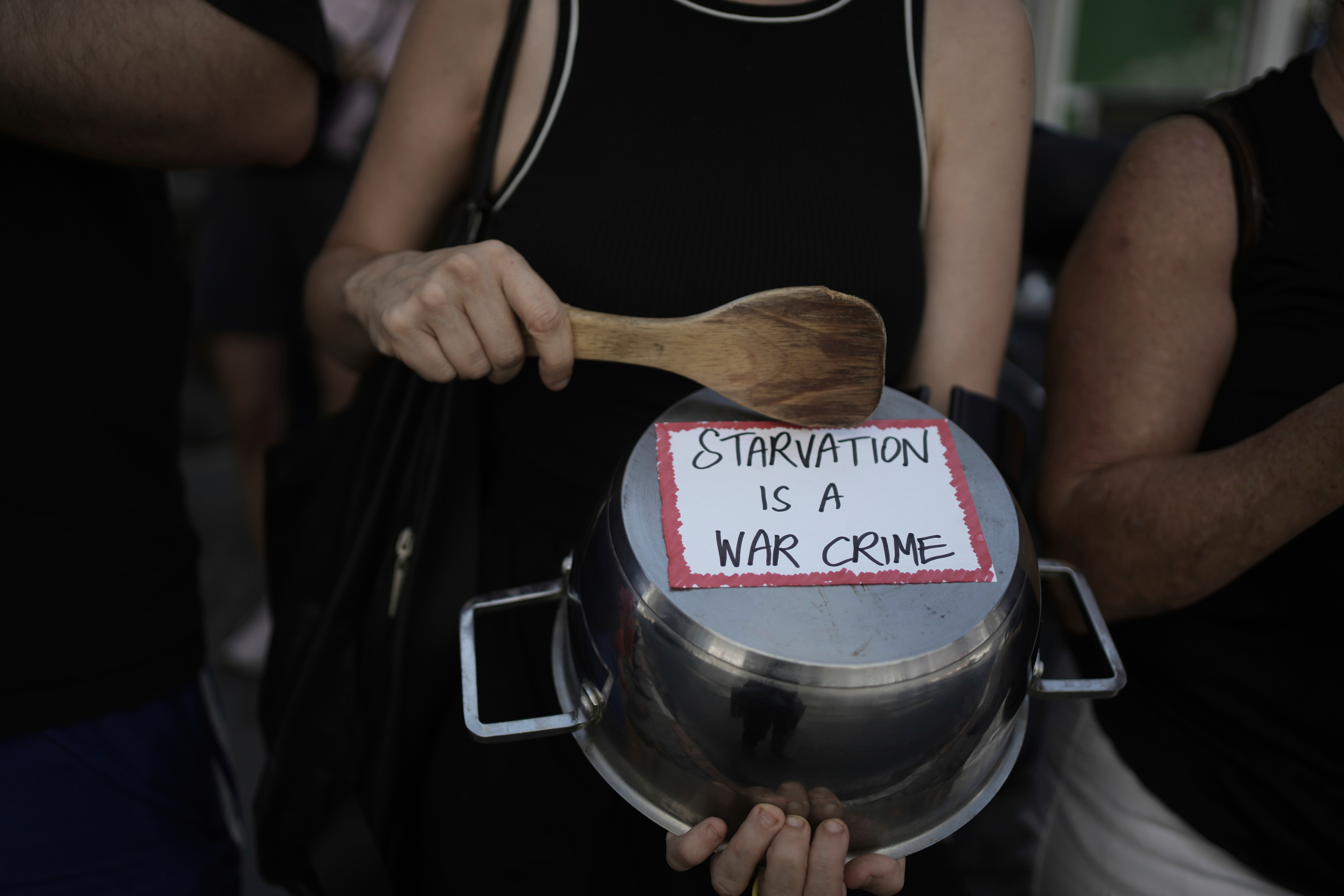 An Israeli activist bangs a pot with a wooden spoon to protest the starvation of Palestinian civilians in the Gaza Strip, outside of the U.S. Embassy branch office in Tel Aviv, Israel, Thursday, July 24, 2025. (AP Photo/Maya Alleruzzo)