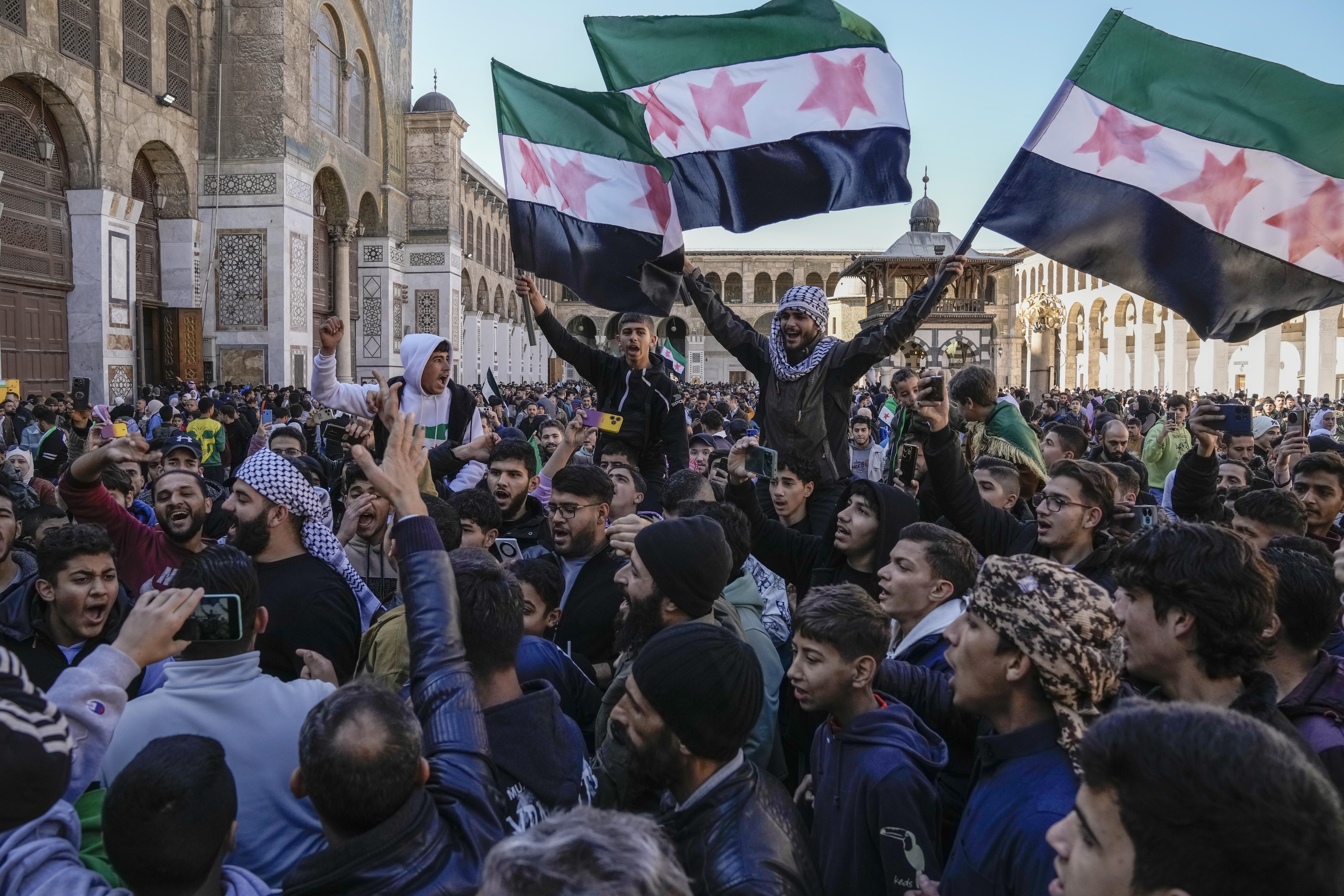 Los sirios corean consignas y ondean la nueva bandera siria mientras se reúnen para las oraciones del viernes en la mezquita omeya de Damasco.