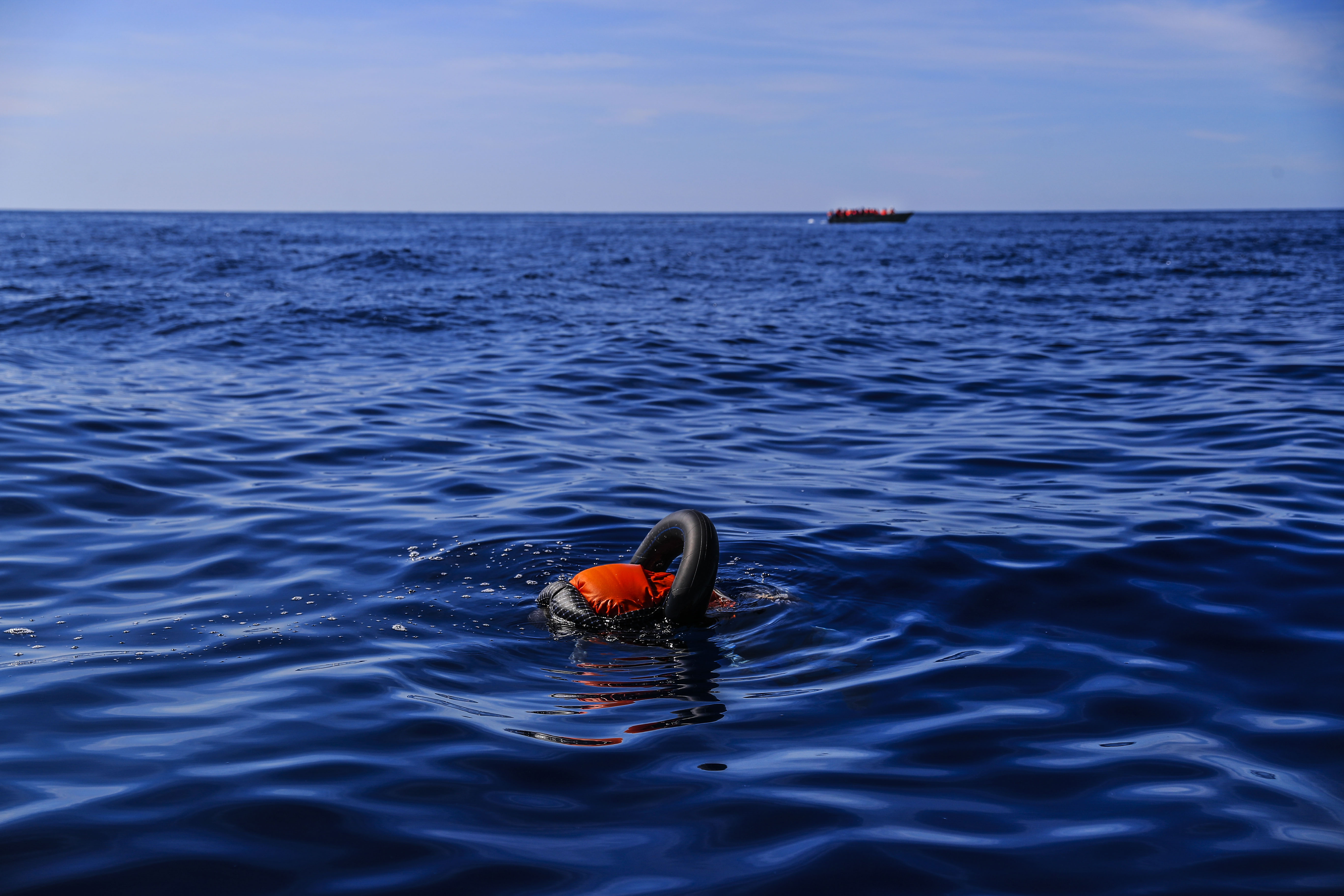 Um afogado flutua no Mediterrâneo enquanto atrás passa um barco com migrantes da Tunísia com destino a Lampedusa (Itália).