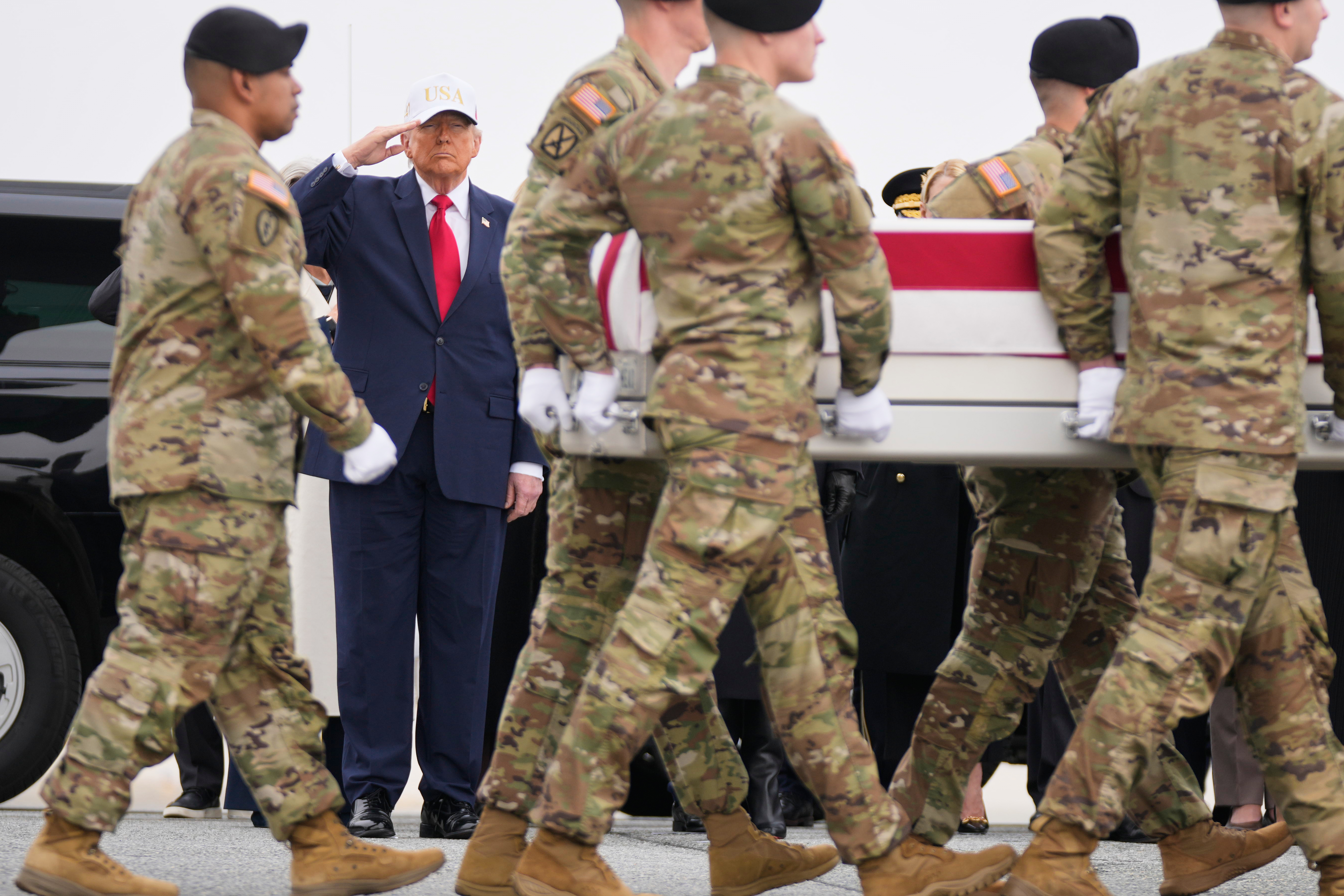 Militares estadounidenses llevan el ataúd de un soldado muerto en Kuwait, atrás, Donald Trump saluda.