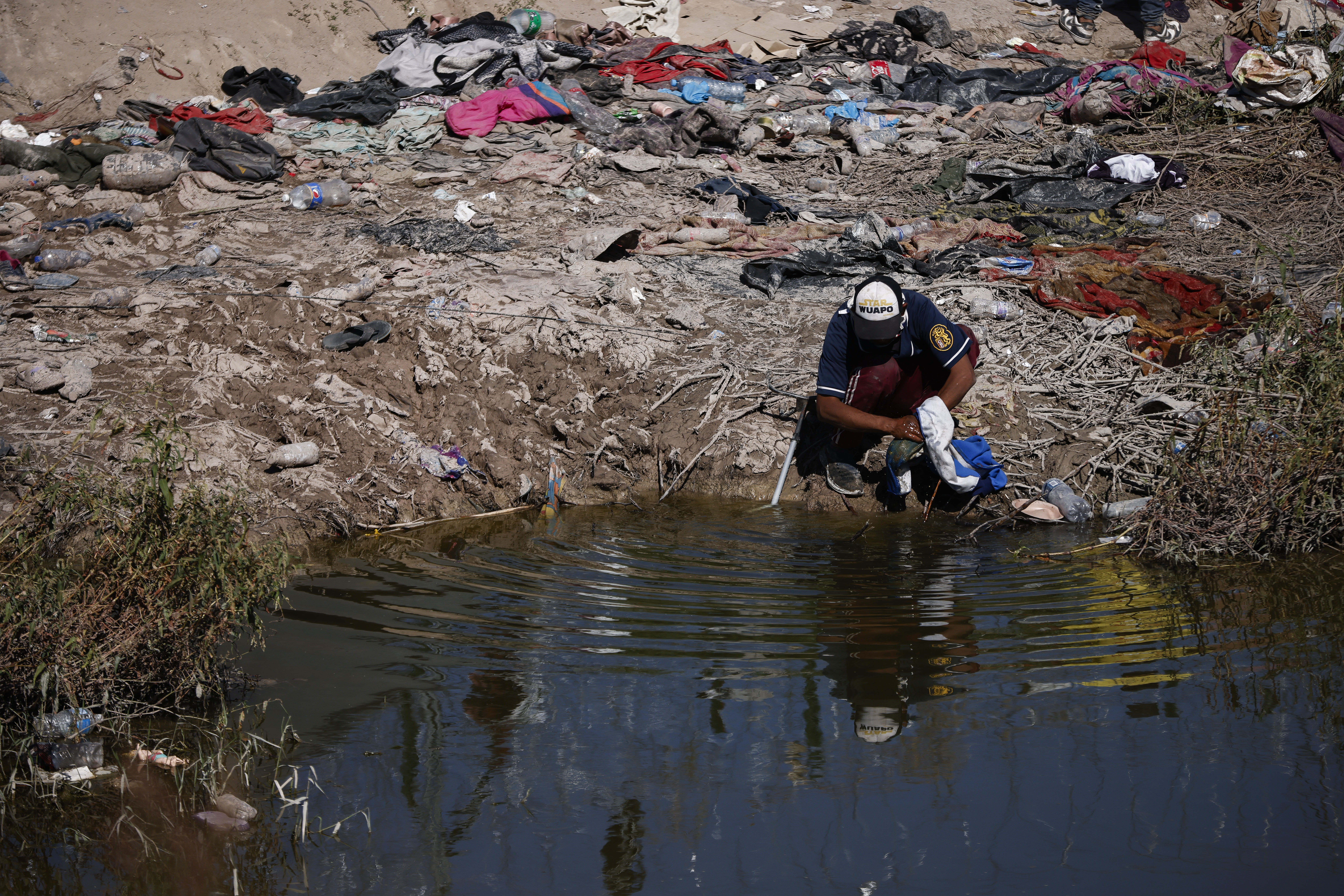 Un migrante lava ropa en el río cerca de la frontera en Ciudad Juárez.