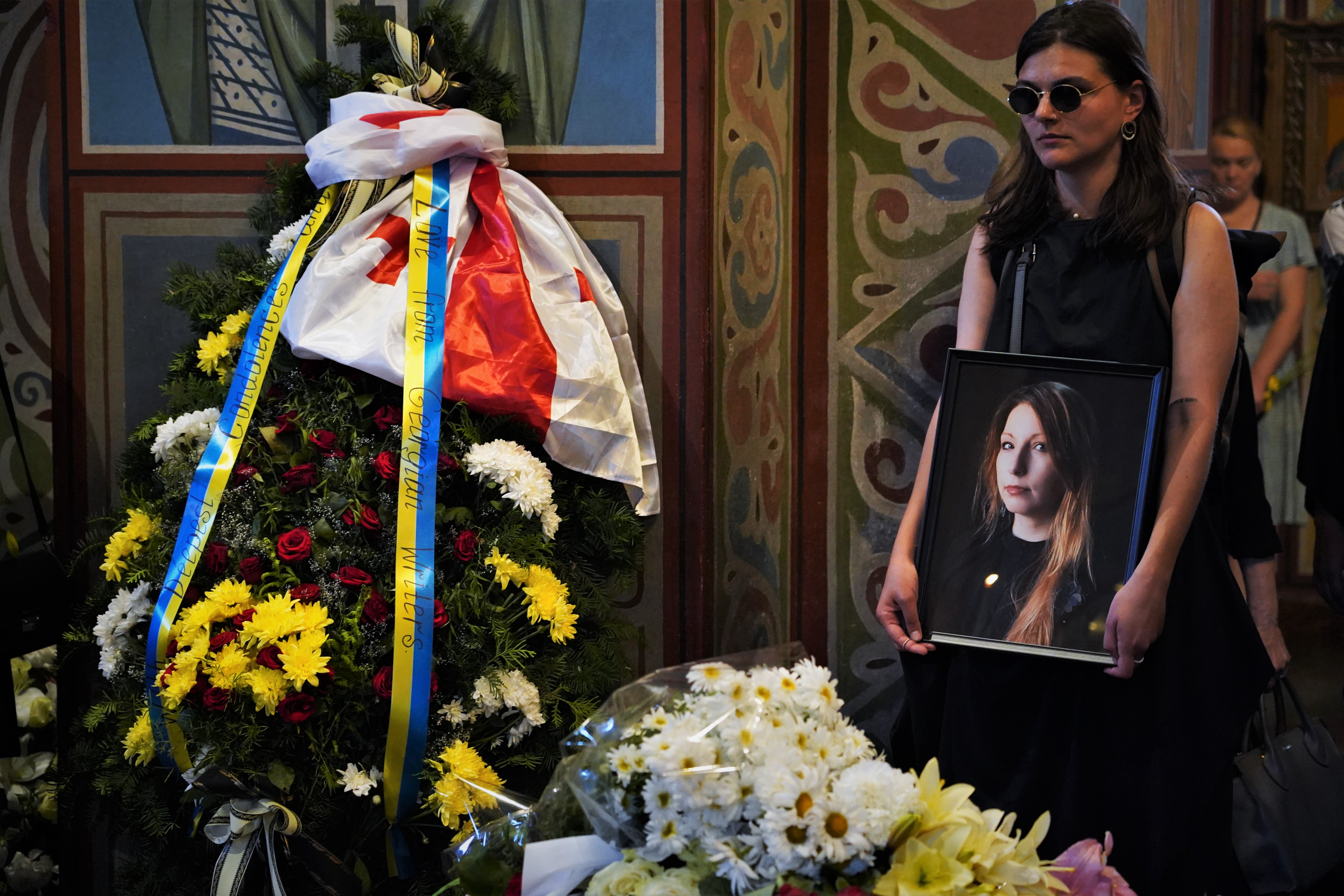 Uma amiga de Victoria Amelina segura seu retrato durante o funeral.