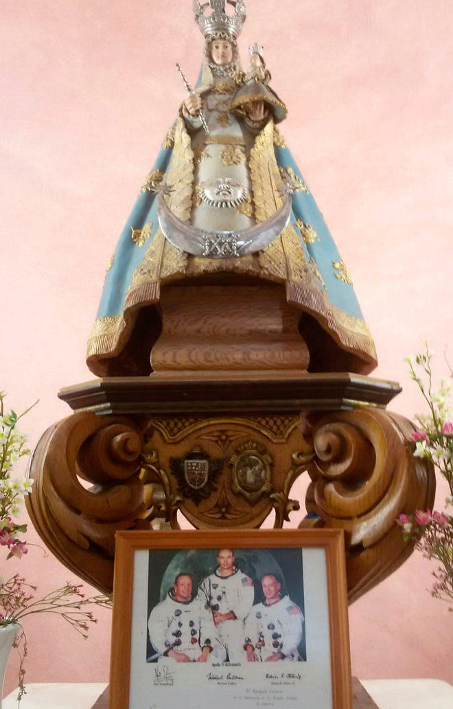 Image of the Virgen de Luna next to the signed photo of the three astronauts who traveled on Apollo XI