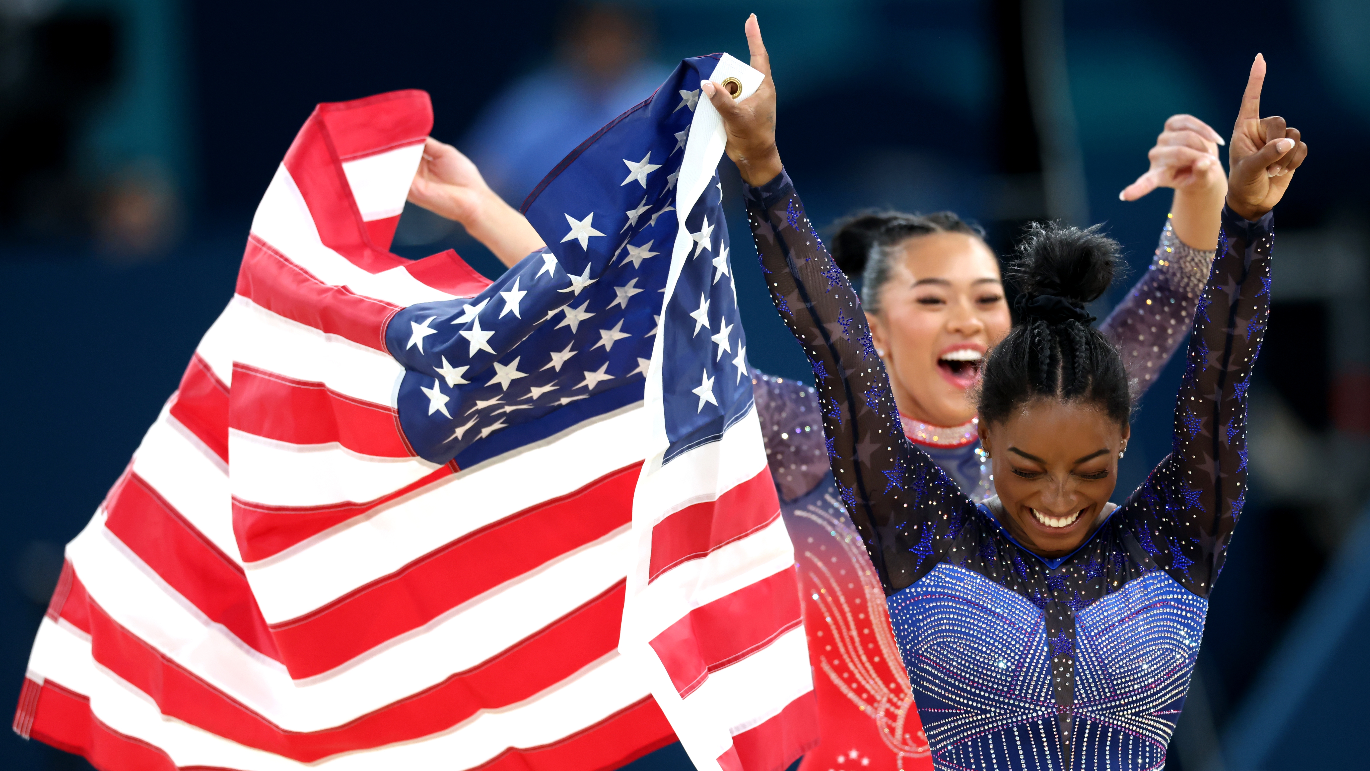 PARIS, FRANCE - AUGUST 01:  Gold medalist Simone Biles and Bronze medalist Sunisa Lee of Team United States celebrate with the American flag after competing in the Artistic Gymnastics Women's All-Around Final on day six of the Olympic Games Paris 2024 at Bercy Arena on August 01, 2024 in Paris, France. (Photo by Pascal Le Segretain/Getty Images)