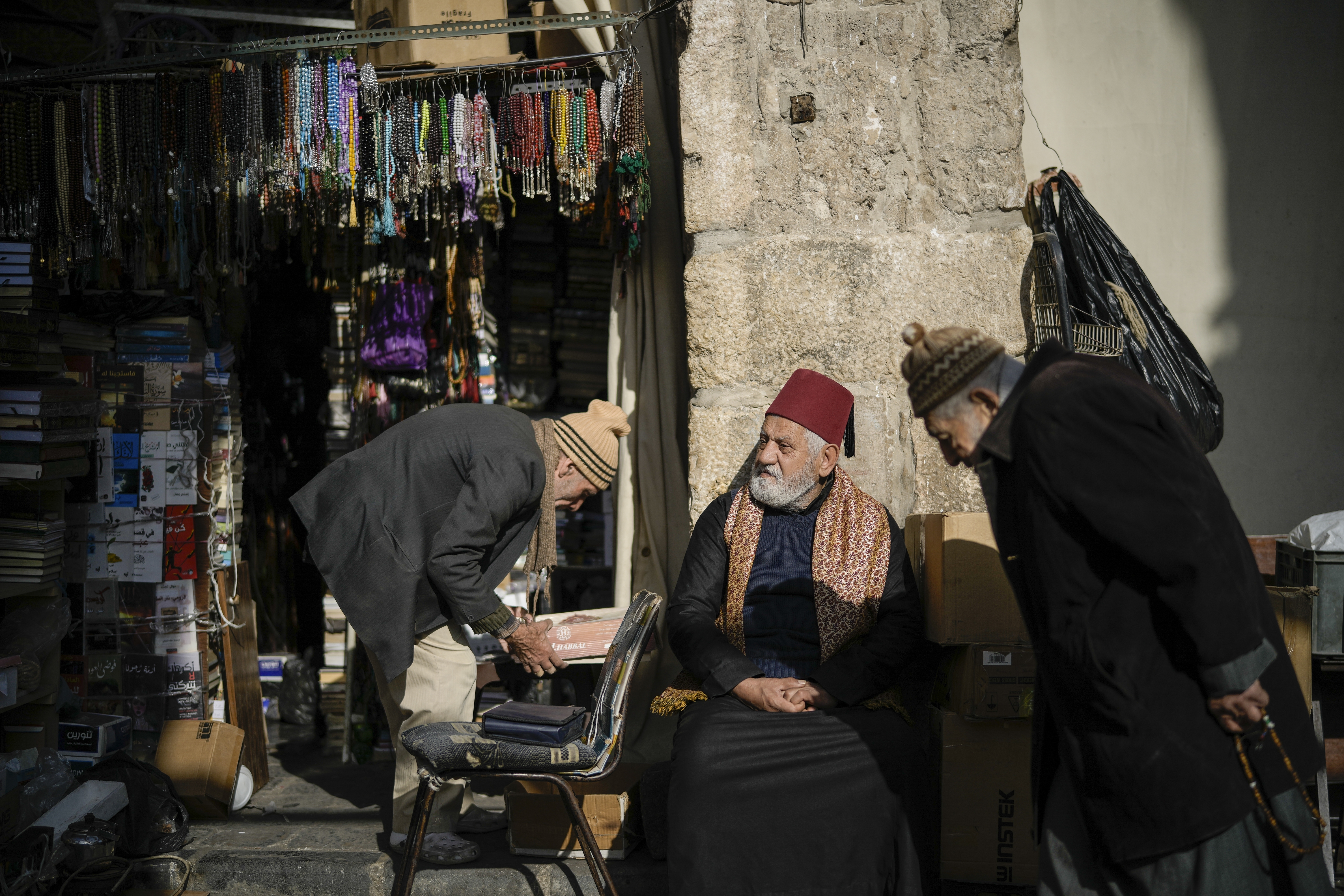 Un hombre se sienta junto a un comerciante que prepara su tienda en la Ciudad Antigua de Damasco, la capital de Siria, este viernes 20 de diciembre de 2024.