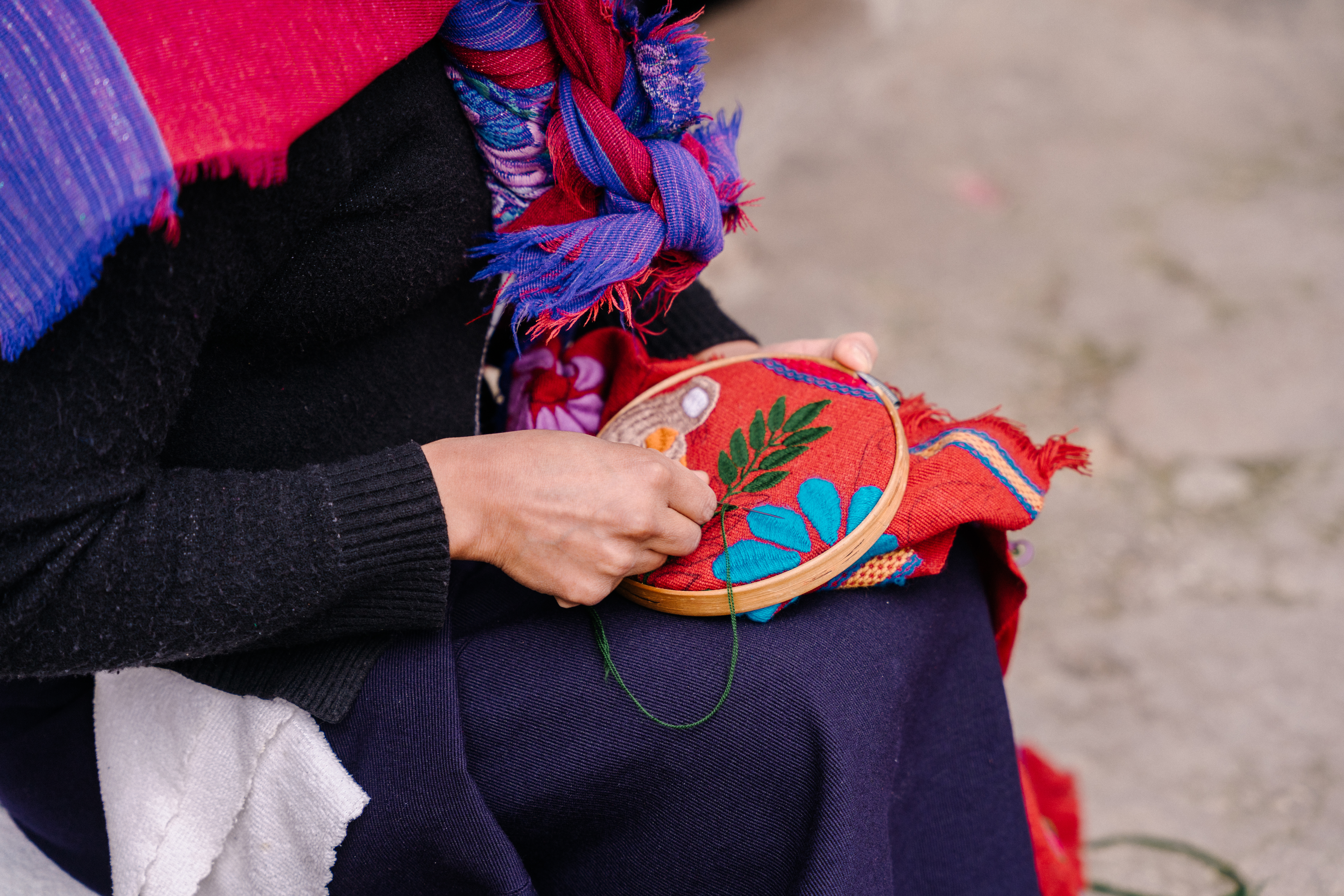 Vista cercana de una mujer bordando motivos florales en un textil granate.