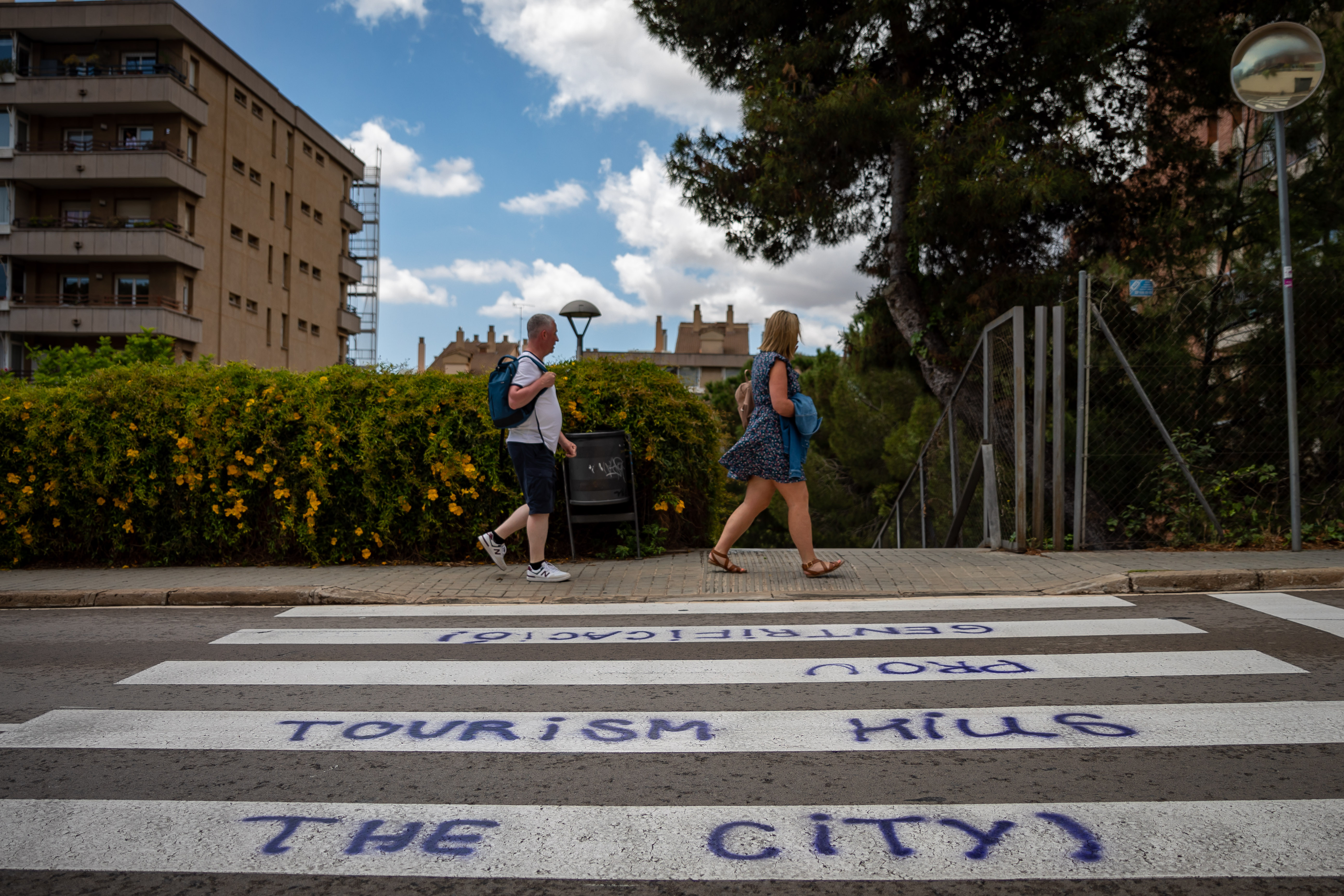 Un par de visitantes de Barcelona caminan ante una pintada en la calle en contra del turismo.