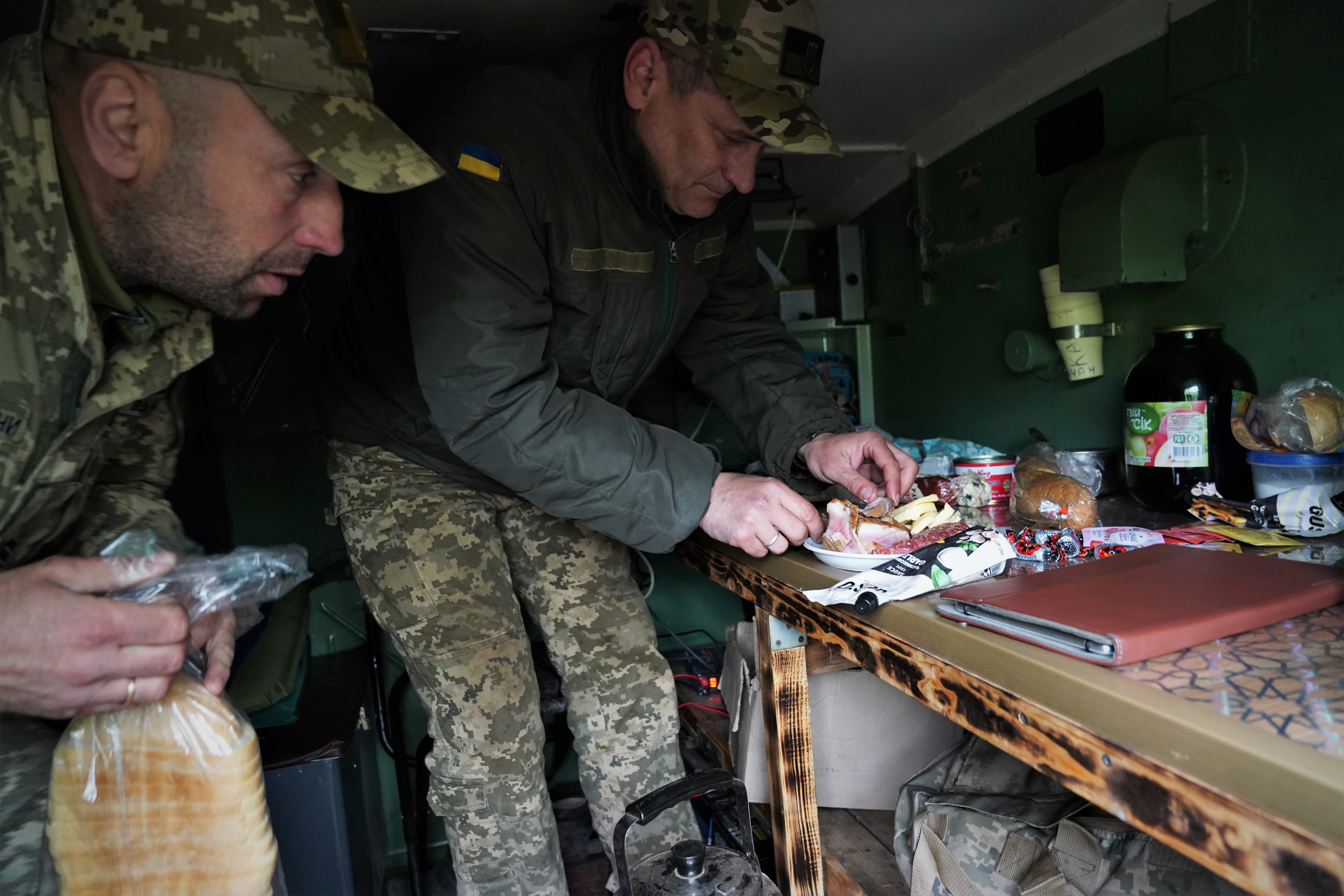 Volodimir (à direita), comandante de uma empresa de lançamento de mísseis grad, prepara algo para comer enquanto espera a ordem de atirar na frente de Chasiv Yar perto de Bakhmut.