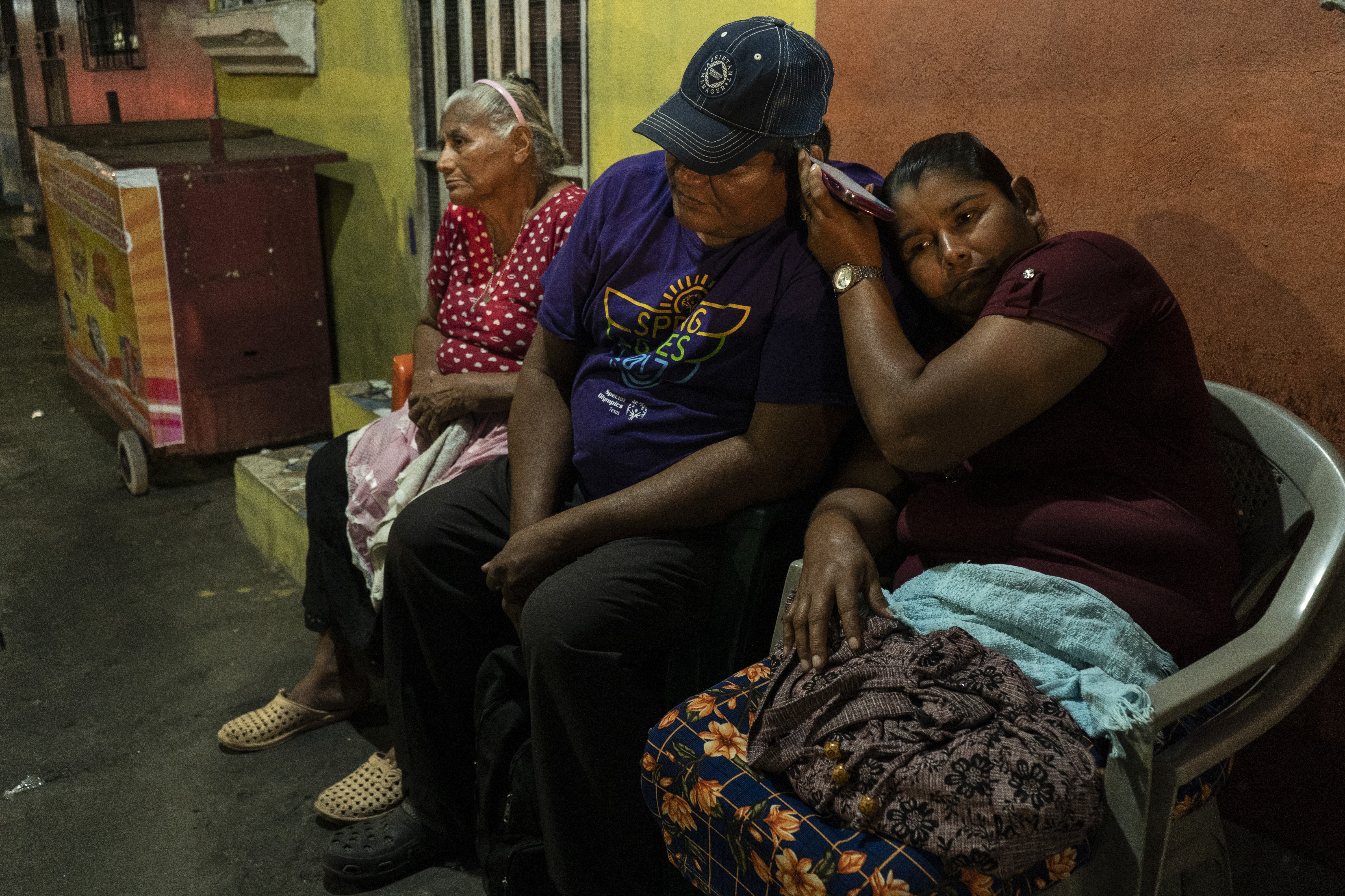 Três pessoas esperam por um familiar detido em frente à sede do El Penalito em San Salvador. 
