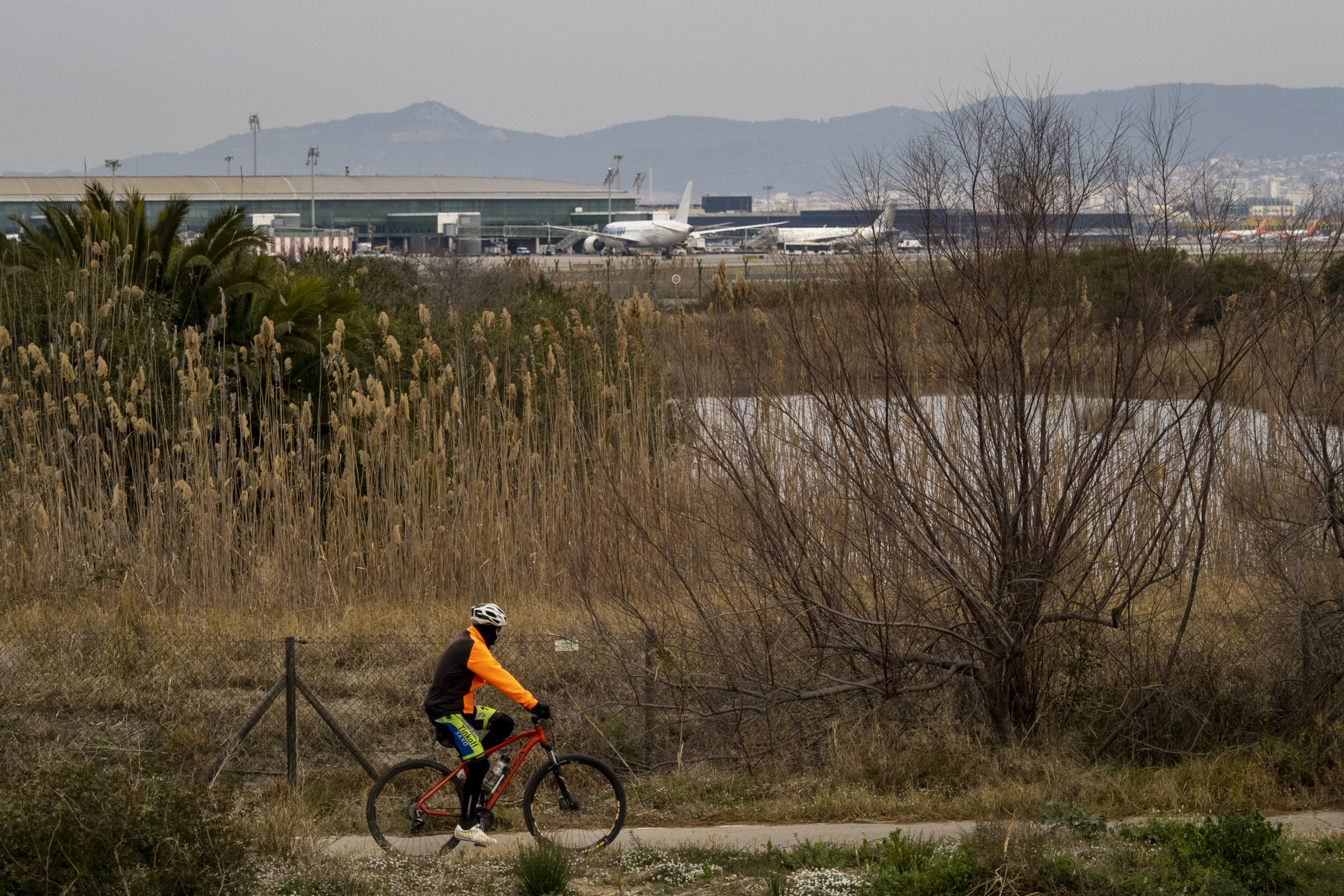 Un ciclista pasa junto a la valla del Aeropuerto del Prat de Barcelona. 