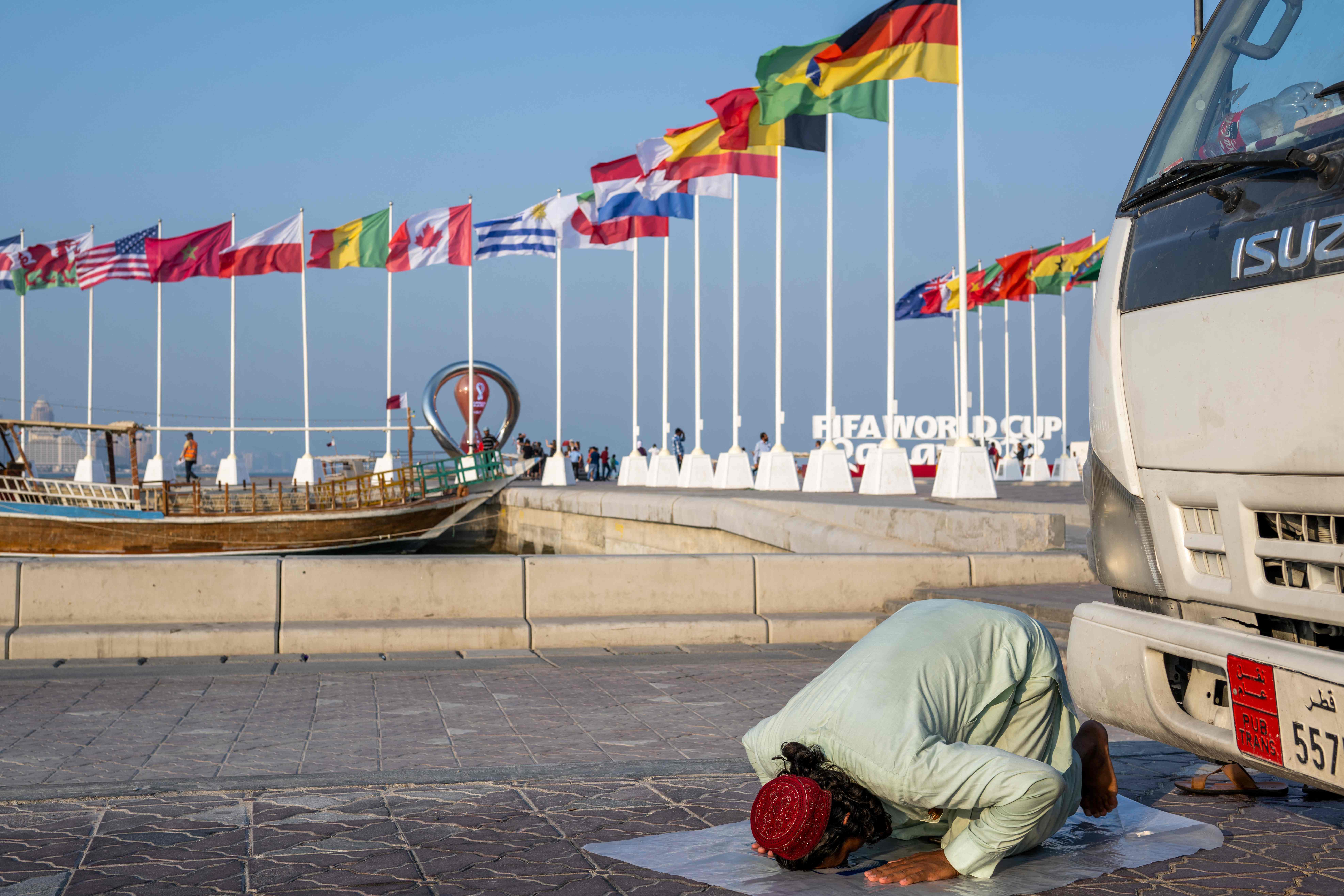 A worker prays near the flags of the World Cup participating countries in Doha. AFP
