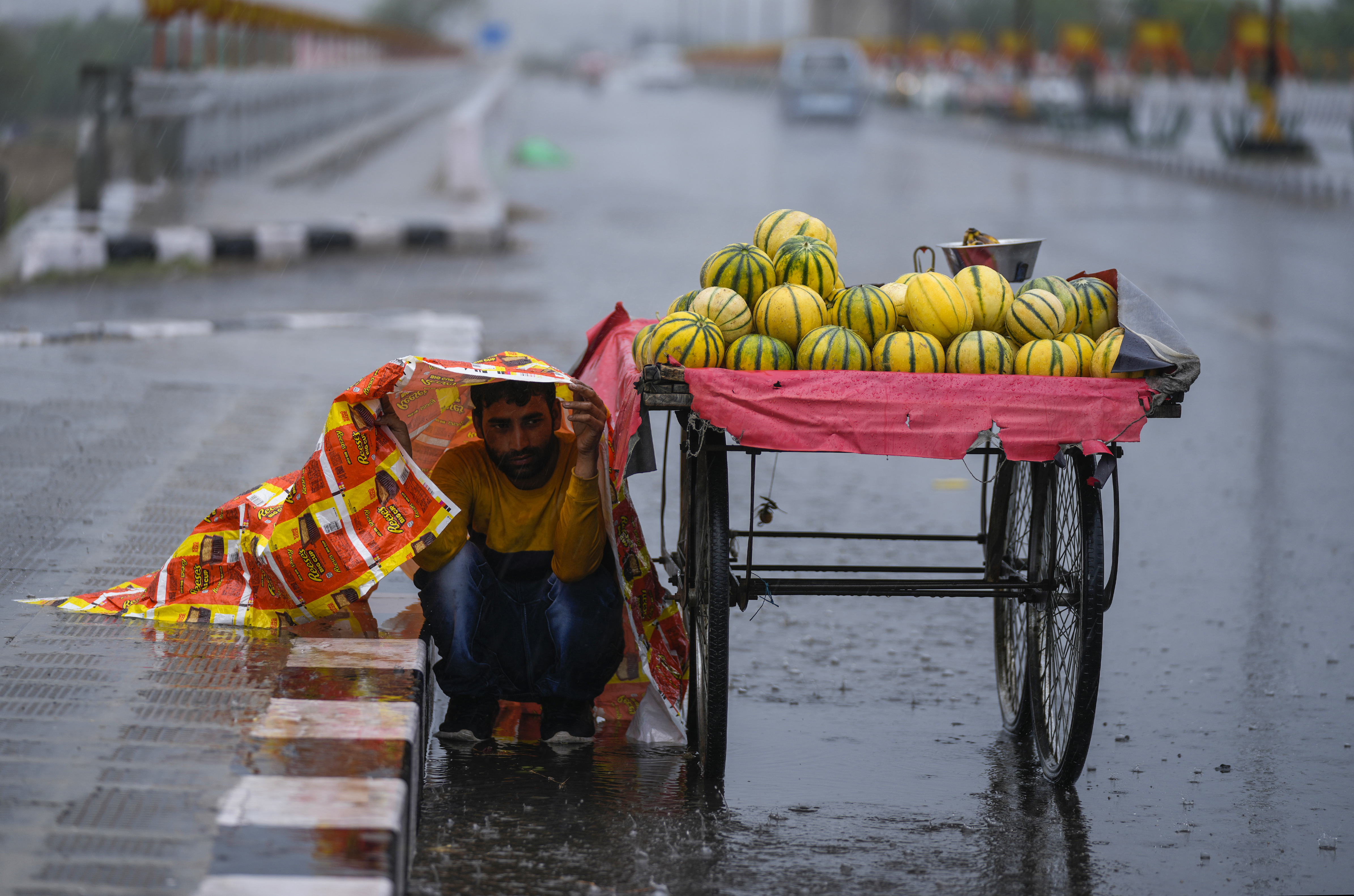 An Indian fruit seller shelters from the rain under a plastic sheet in Jammu. AP