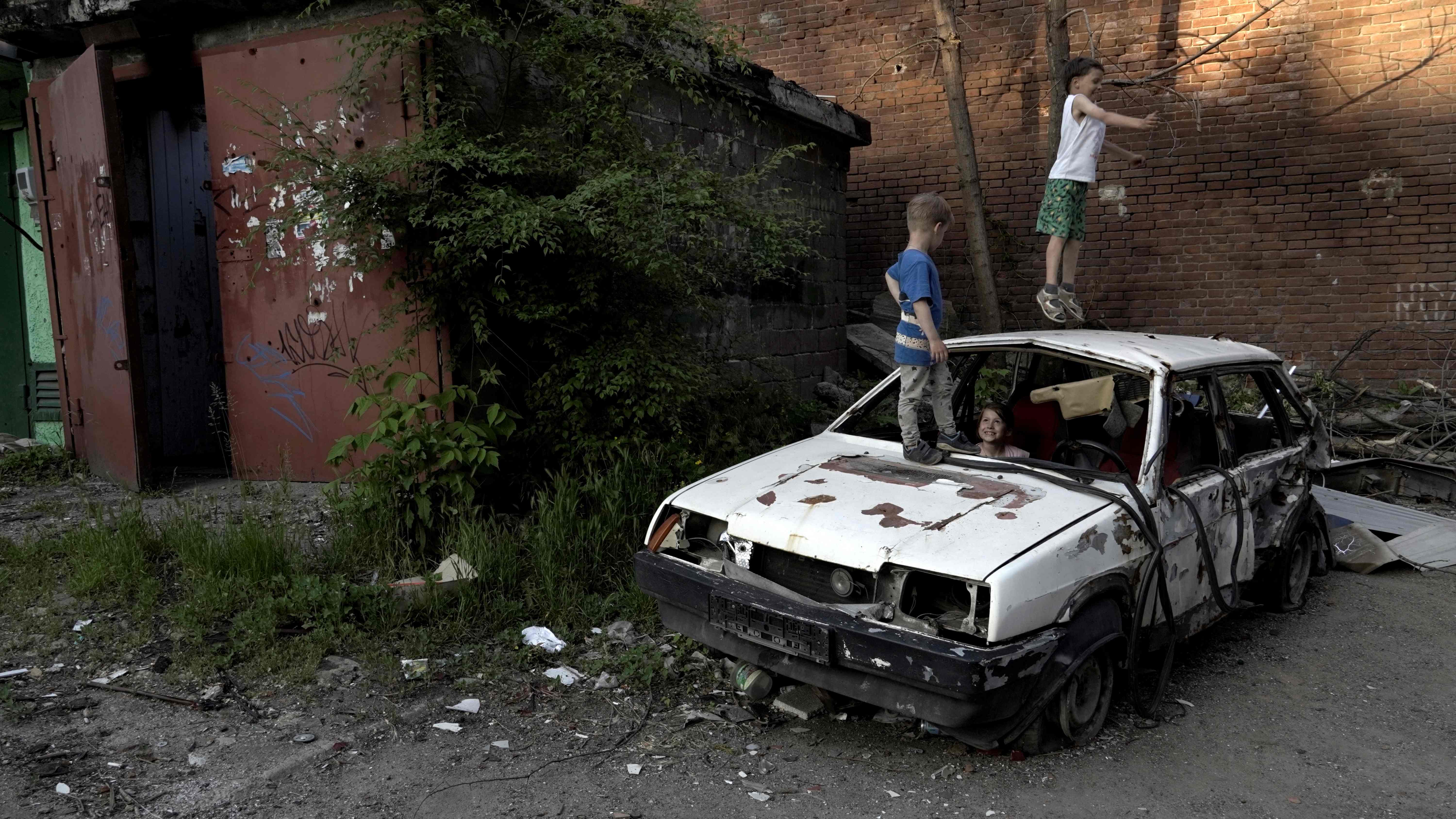 Children play on a destroyed car in a residential area of Mariupol, amid the Russian invasion of Ukraine. AFP