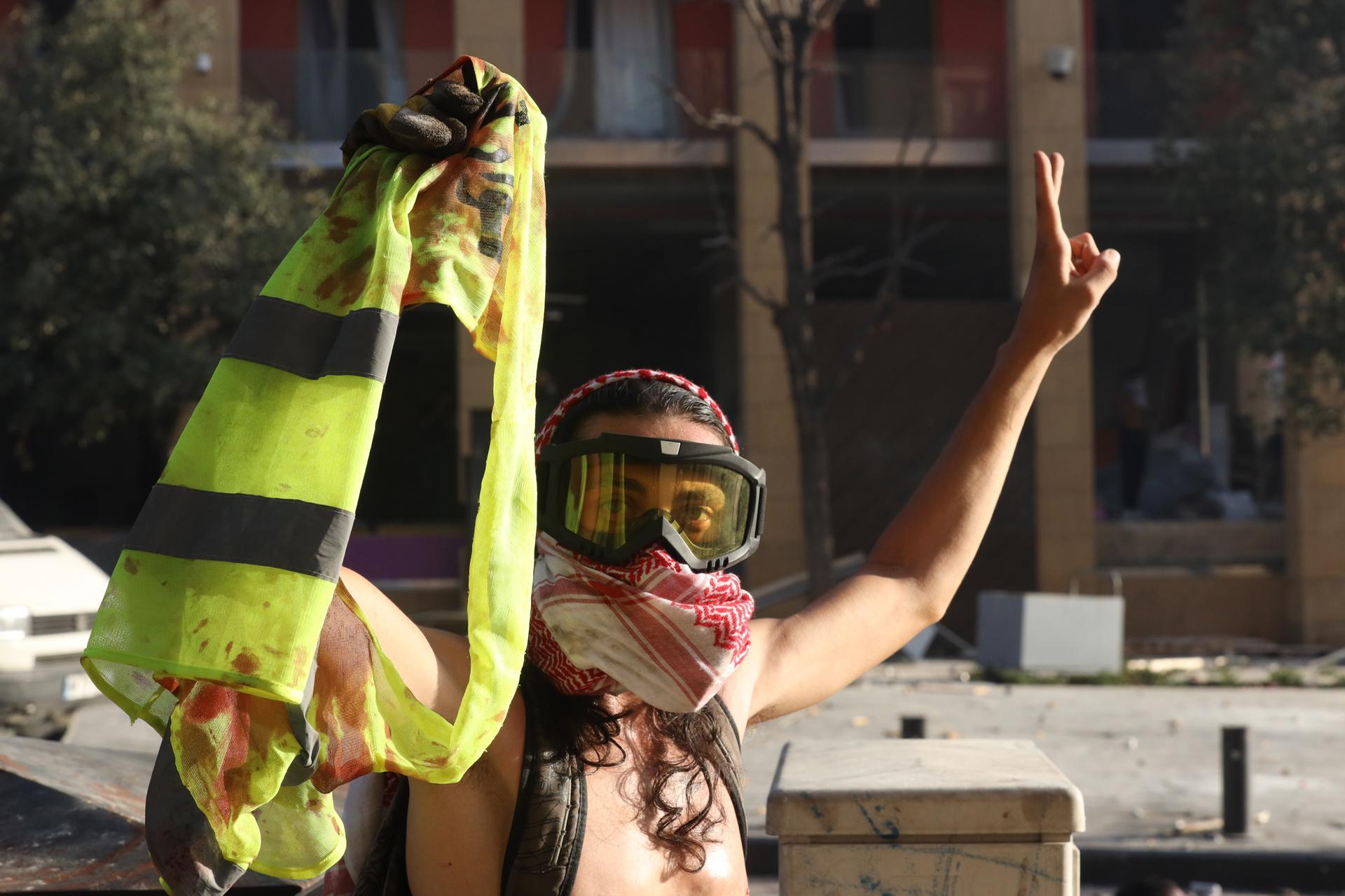 A Lebanese anti-government protester flashes a victory sign and holds a blood-stained yellow jacket of a fellow protester during clashes with riot police. EPA